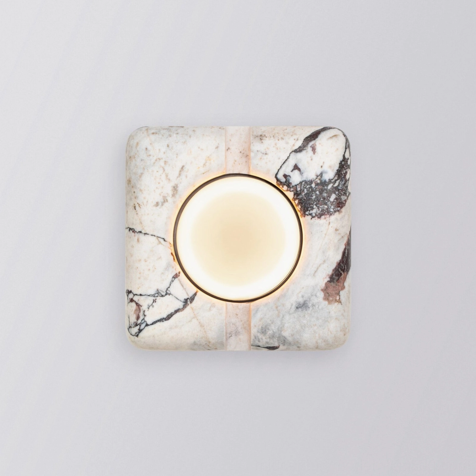 Modern marble wall lamp illuminated with warm LED light glowing from central glass lens