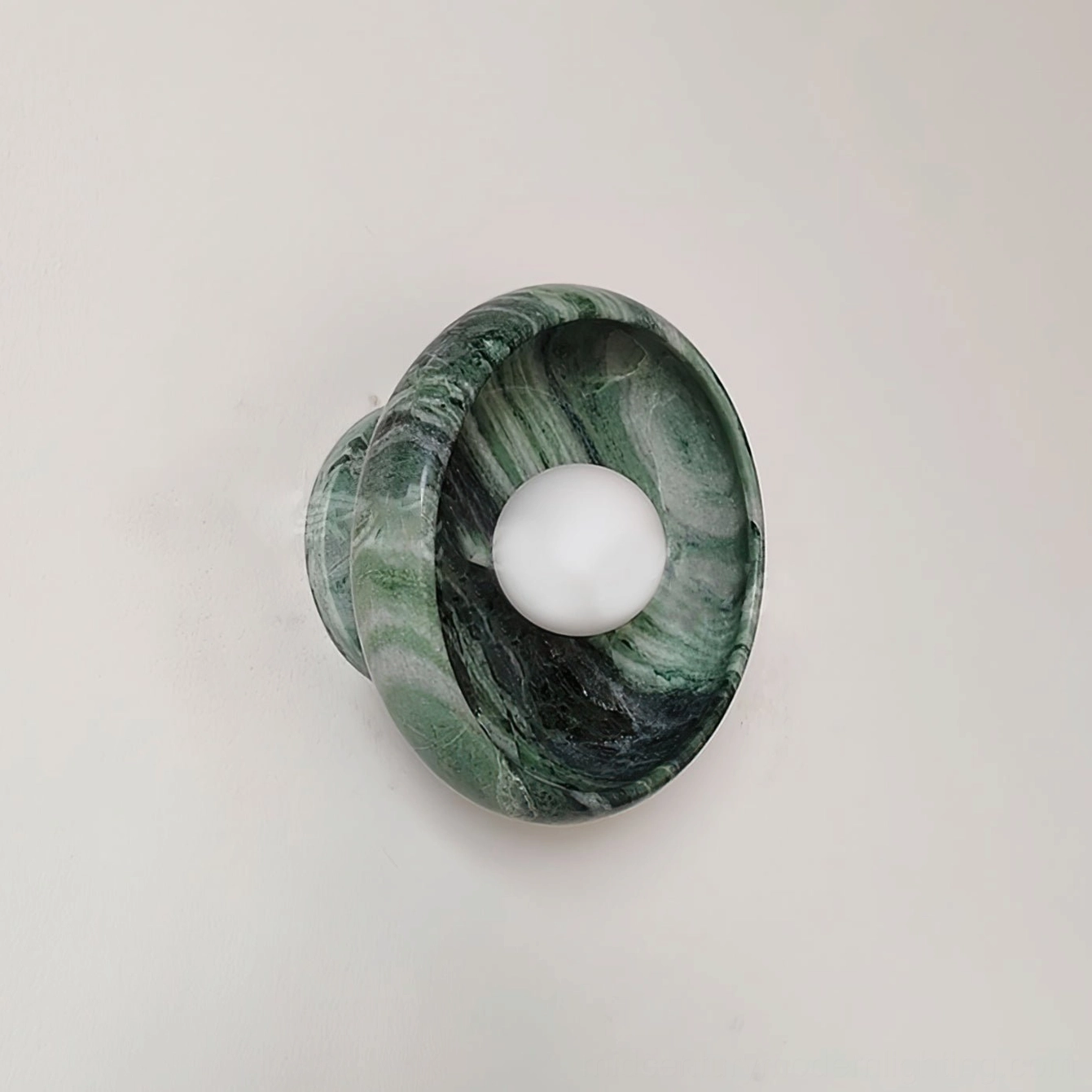 Mid-century modern marble wall lamp three-quarter view, compact round dark green stone fixture on gray background