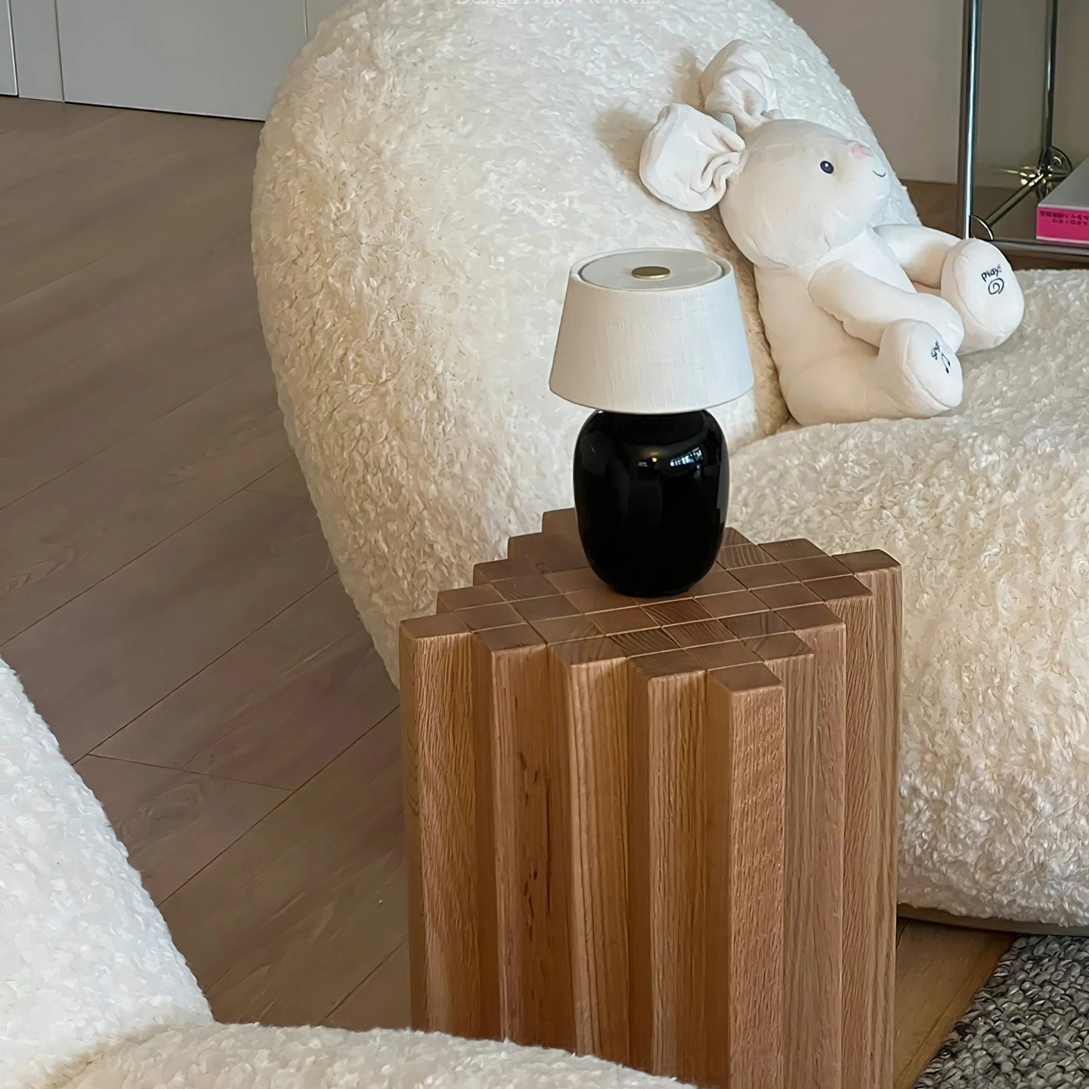 Black ceramic Marie table lamp on striped wooden side table next to modern boucle sofa