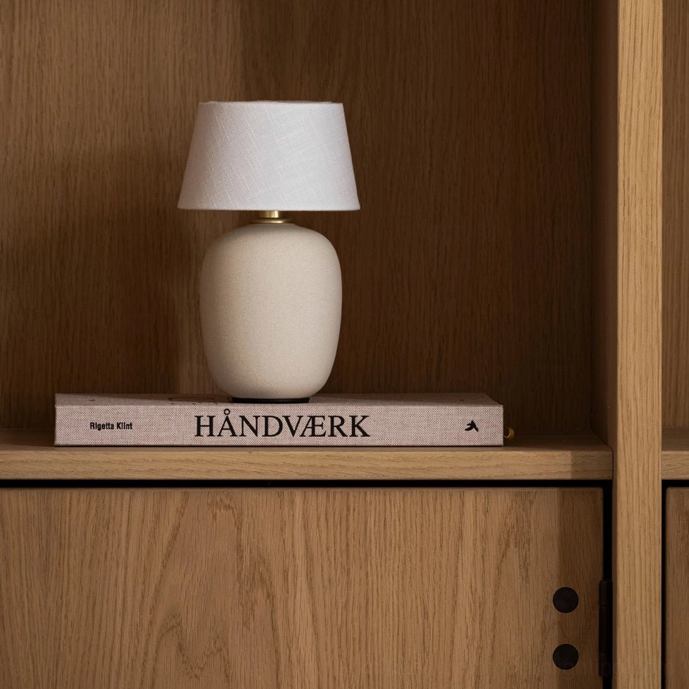 Beige Marie table lamp displayed on decorative book on oak wood cabinet shelf