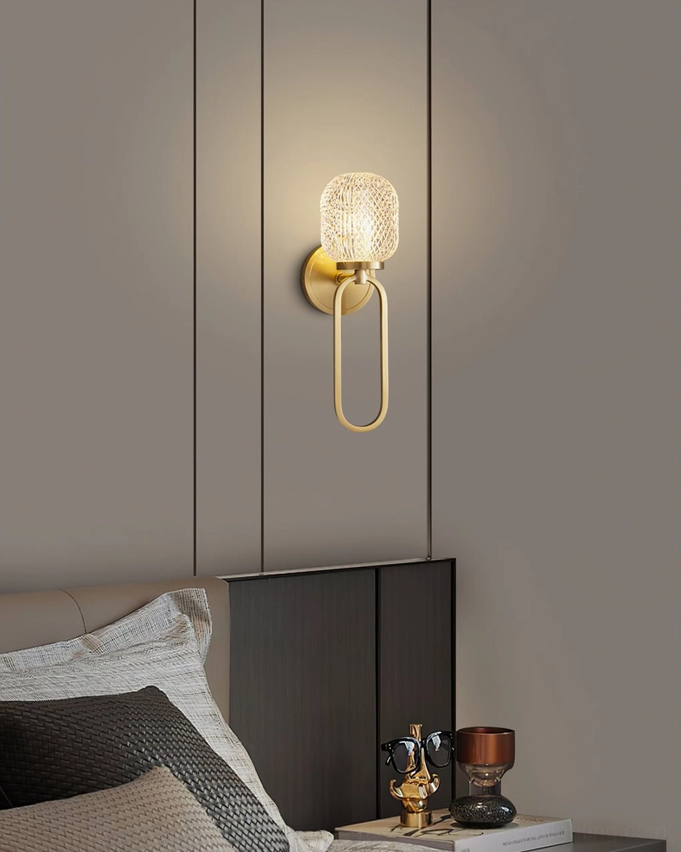 Marni Modern Wall Sconce distant view in bedroom with bed and bedside table - brass loop bracket with cylindrical textured glass