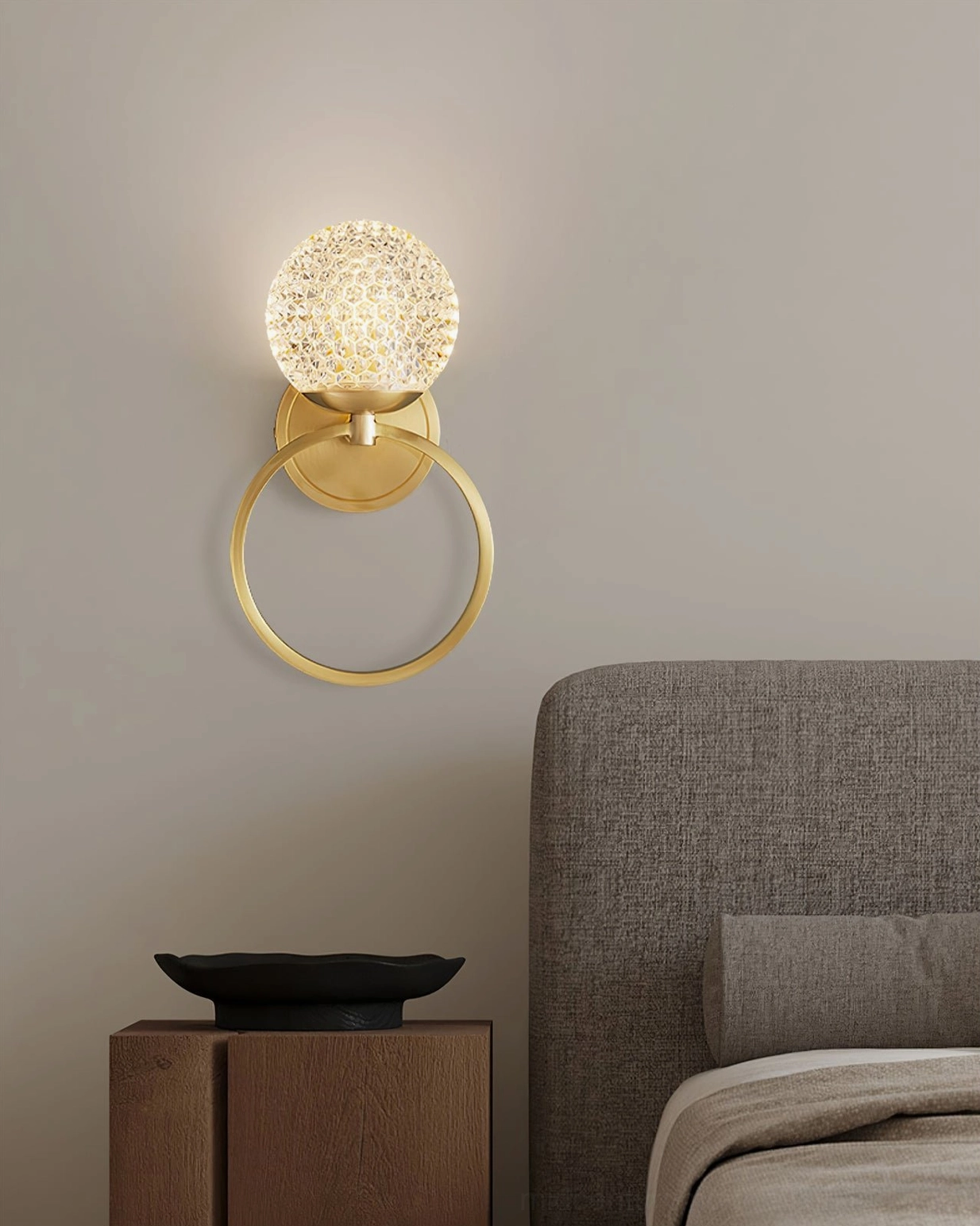 Marni Modern Wall Sconce installed in contemporary bedroom with gray fabric bed and wooden nightstand - brass and crystal fixture