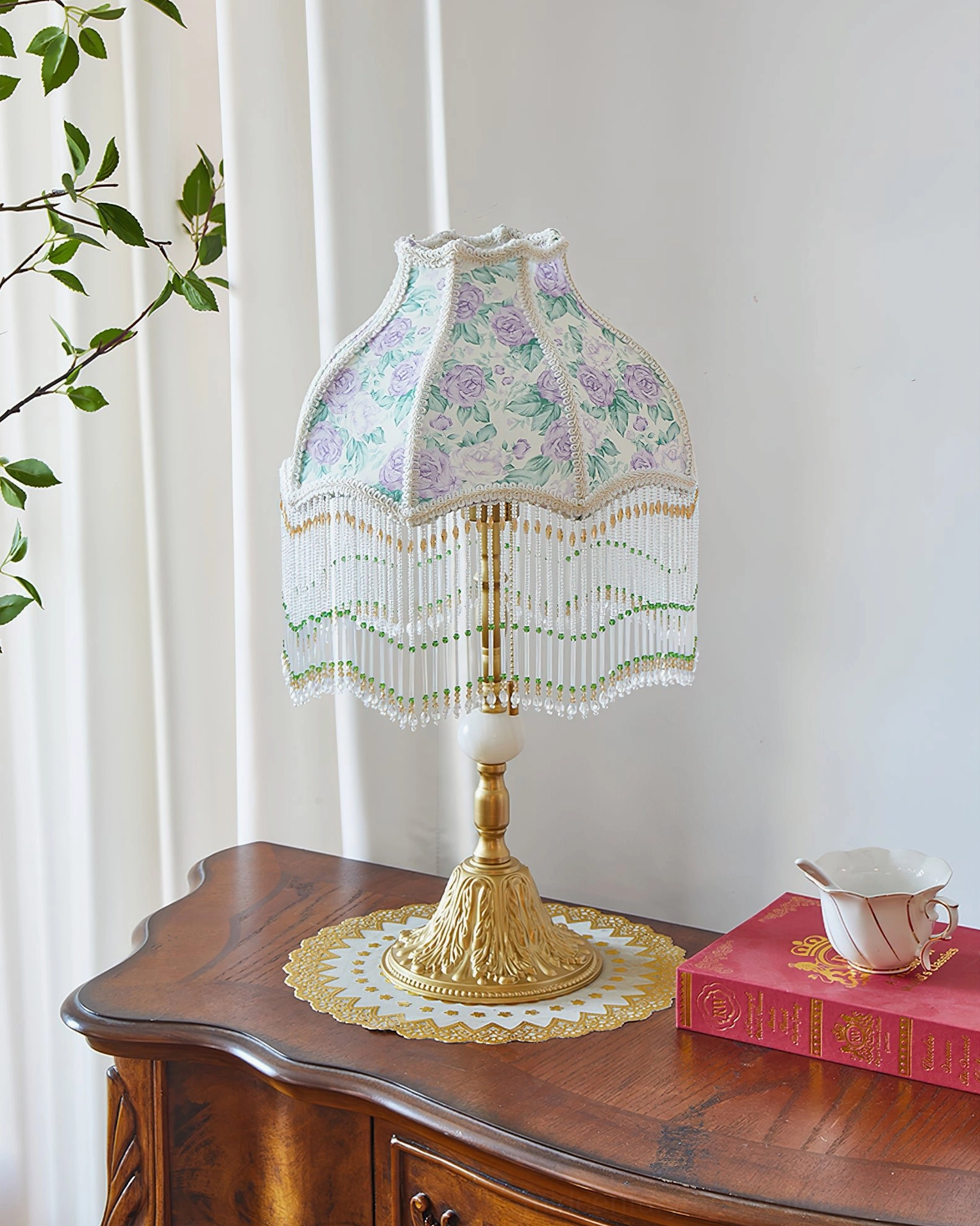 Masa floral table lamp displayed on lace doily with vintage wooden side table styling and decorative book and teacup