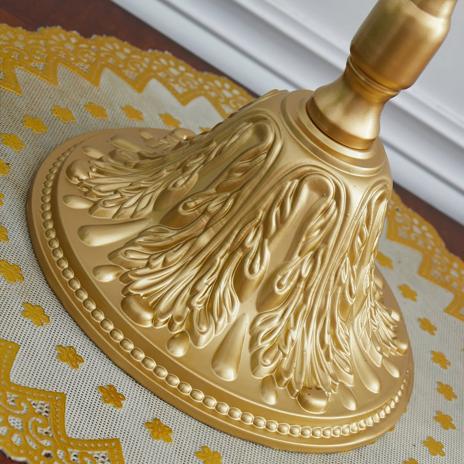 Close-up detail of Masa table lamp ornate carved gold metal base with intricate floral design on lace doily surface