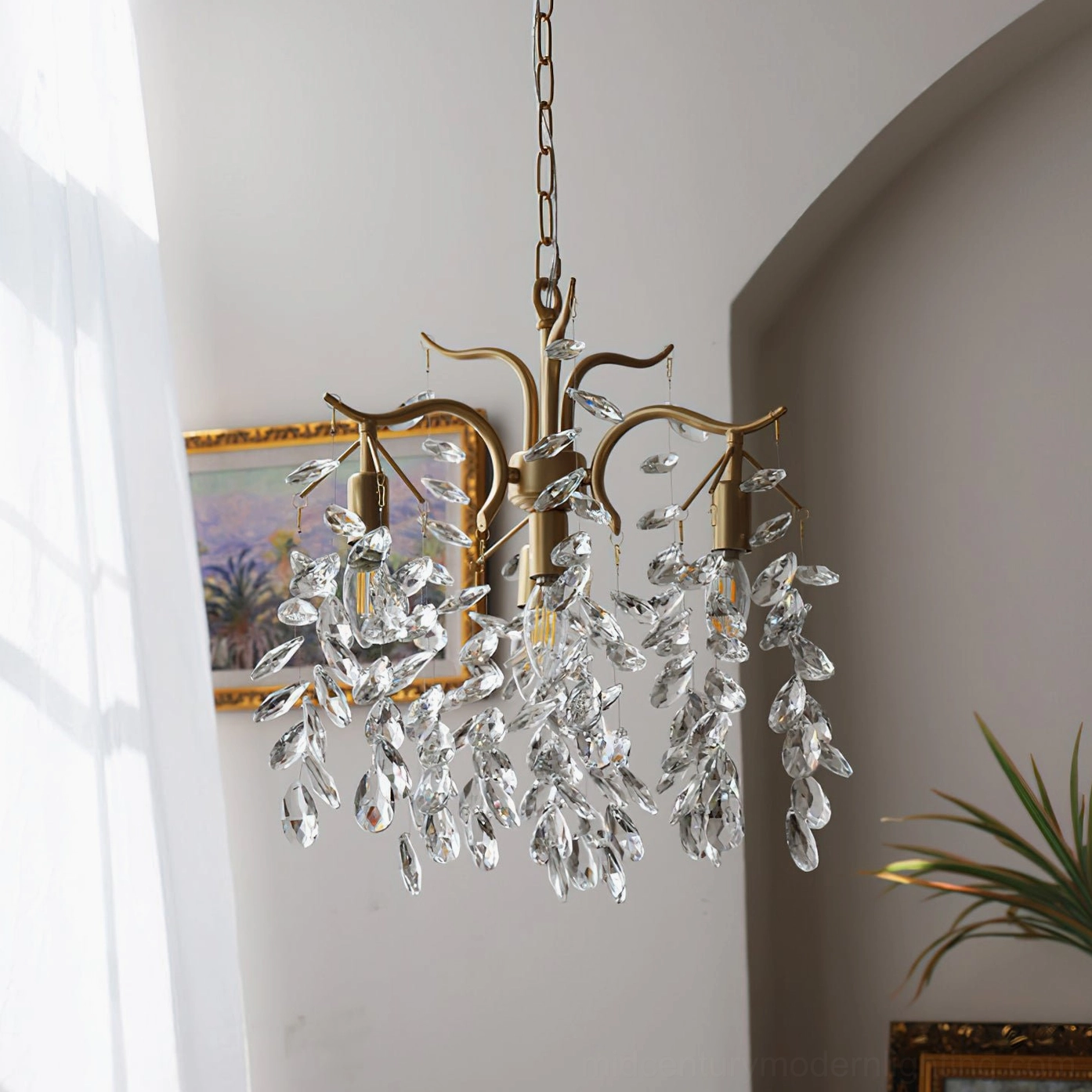 Mid-century modern crystal leaf chandelier side angle view in sunlit home with abstract wall art and natural plant decoration