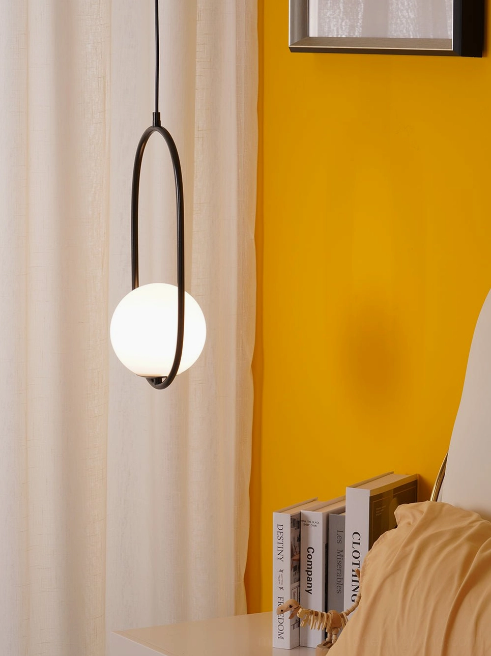 Mila black frame pendant light with warm glass globe shade in Nordic minimalist bedroom corner with decorative books and indoor styling