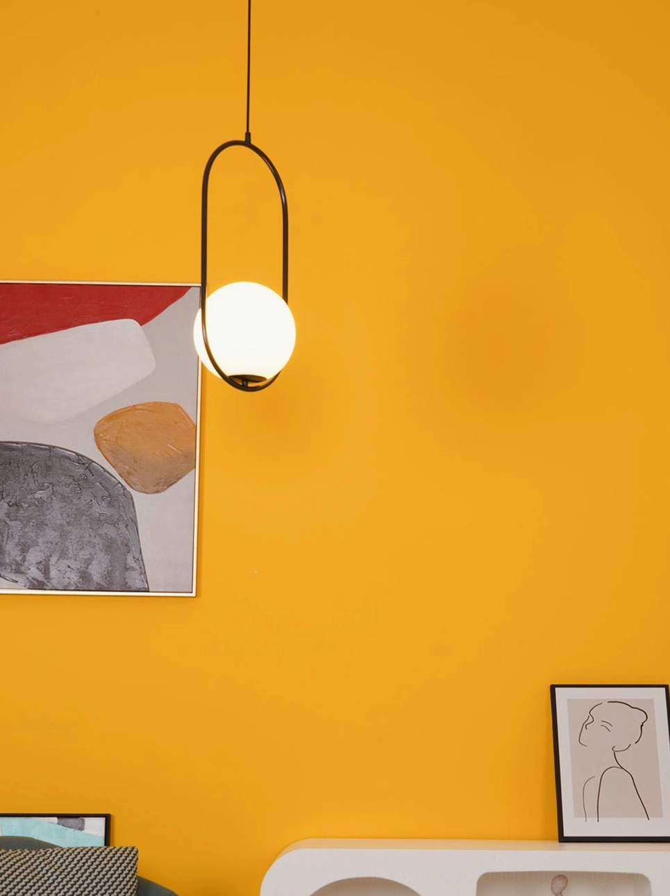 Mila oval pendant light in black metal frame with frosted white glass shade in modern indoor space with orange accent wall art installation