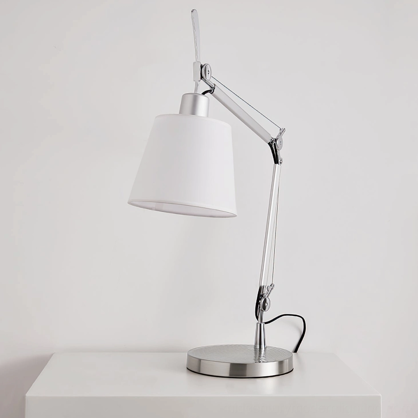 Modern table lamp on white dresser top, showcasing silver metal base and clean minimalist aesthetic from front angle