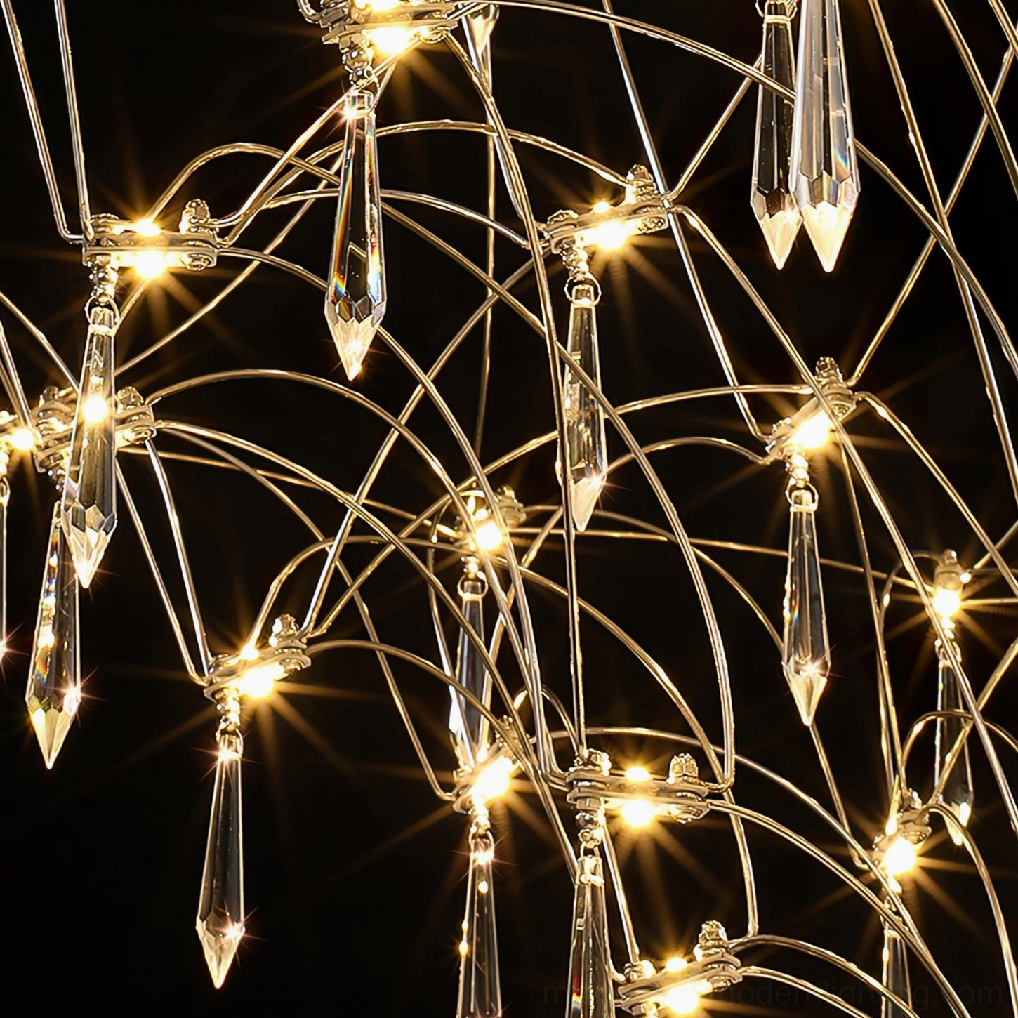 Mira crystal chandelier close-up macro shot showing glowing integrated LED bulbs and delicate stainless steel wiring detail against black background