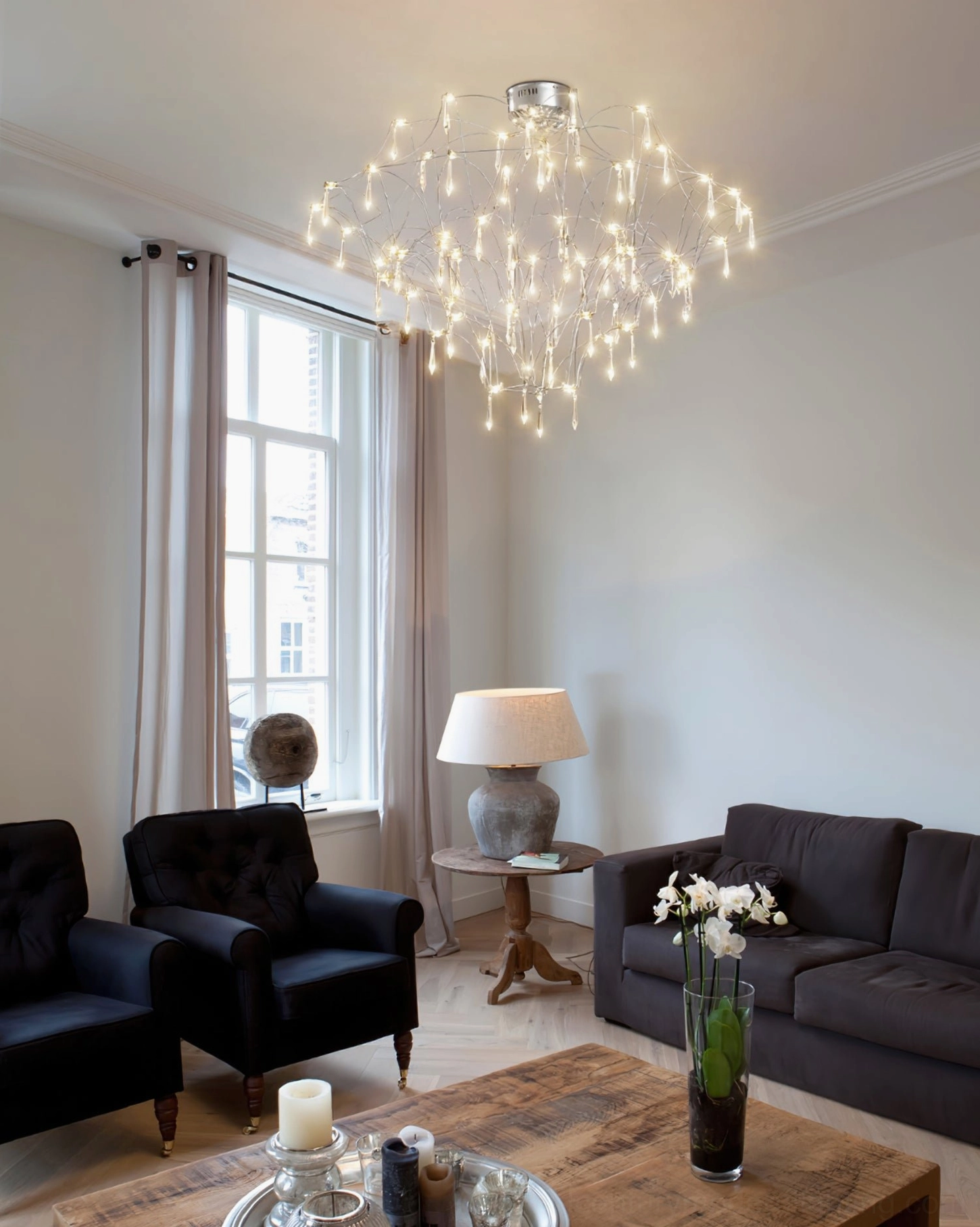 Mira modern crystal chandelier in formal contemporary living room with dark sofa and wooden coffee table, wide room perspective