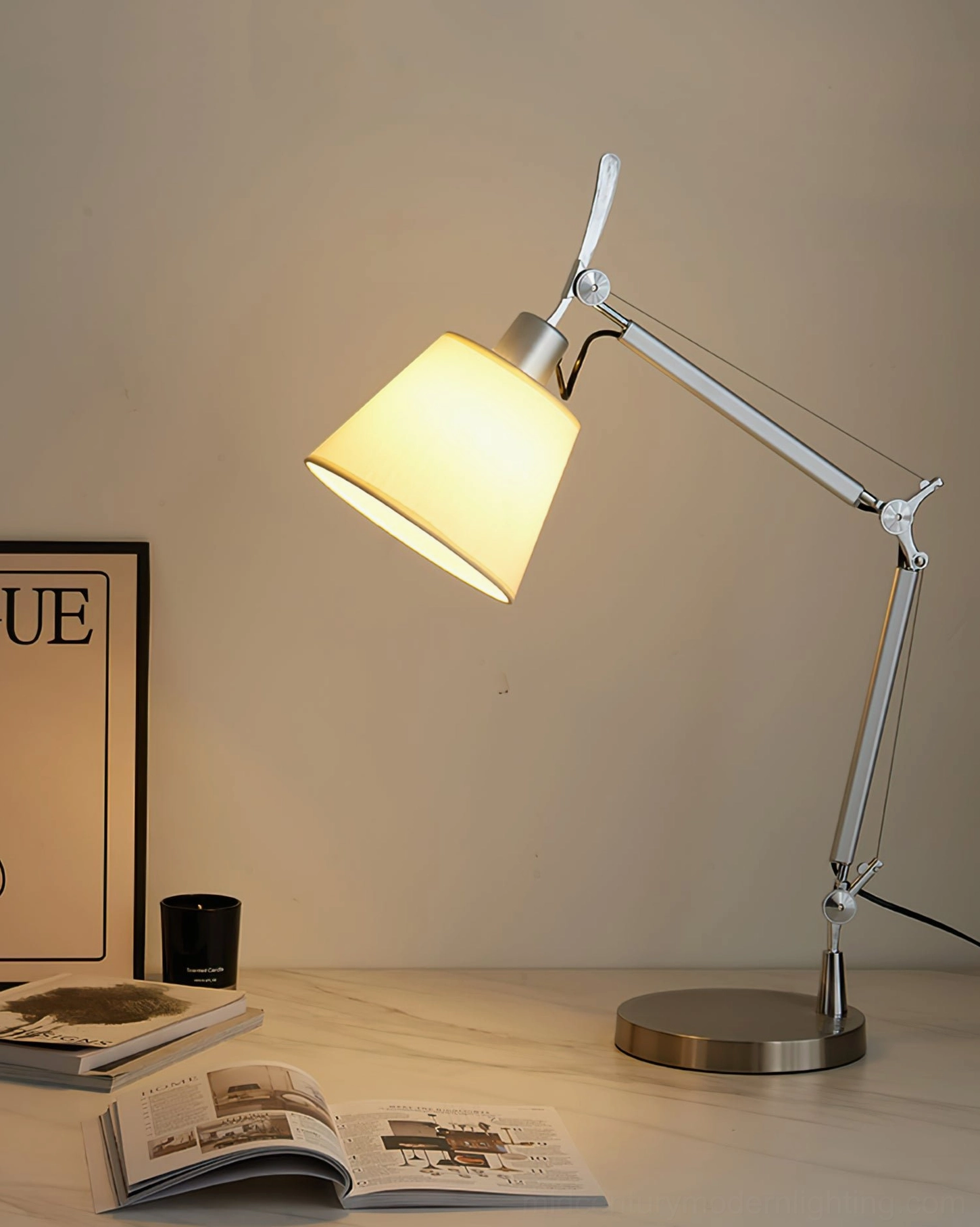 Contemporary adjustable table lamp lit in warm white glow, positioned on desk with decorative poster and magazines for home setting