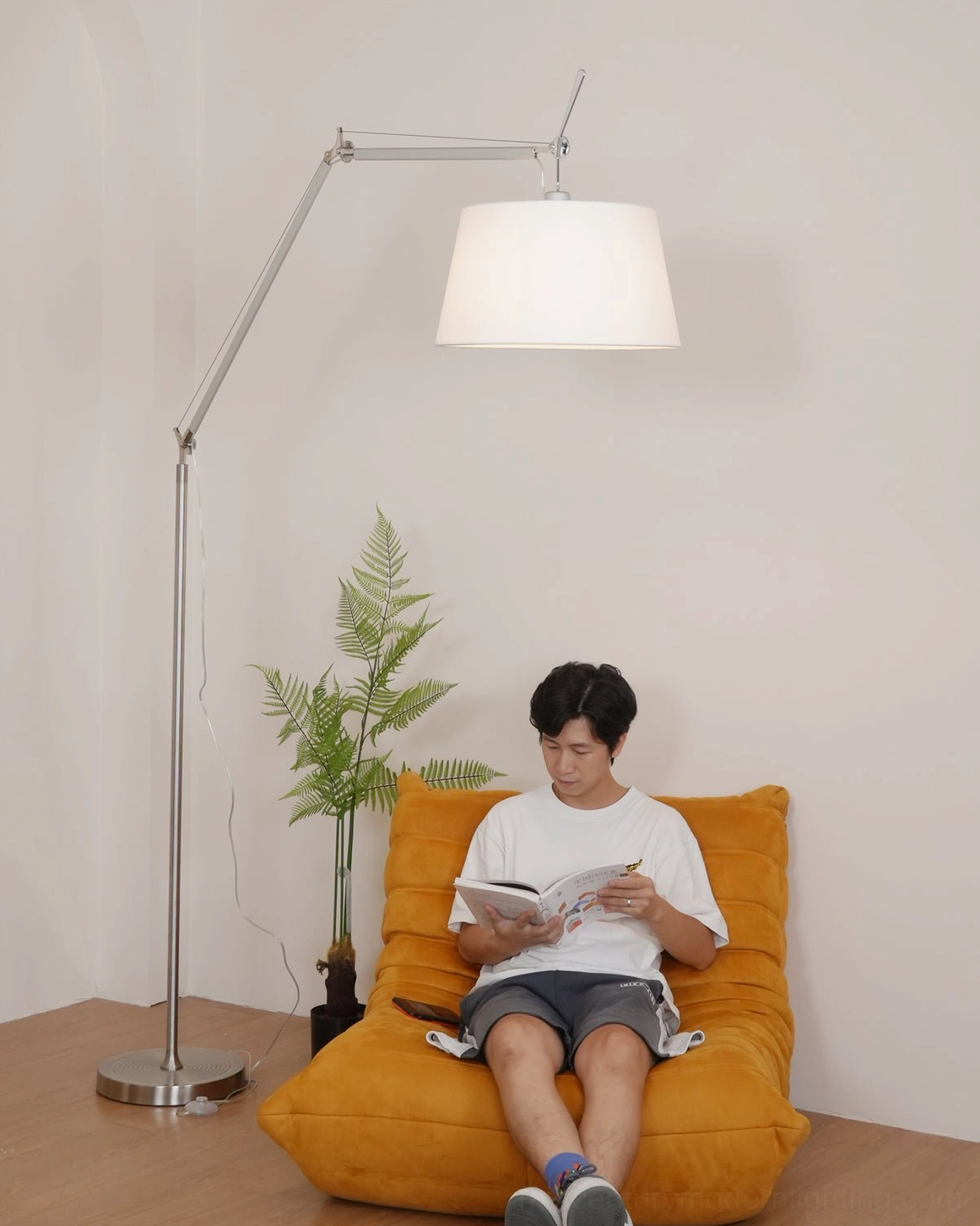 Modern articulating floor lamp in styled living space, silver metal arm positioning and white shade ambient lighting