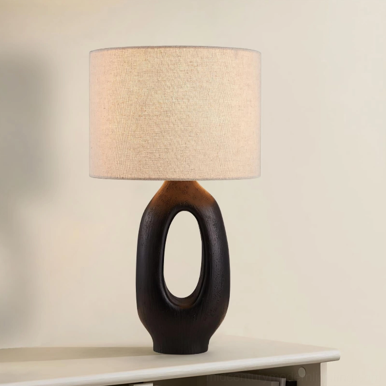 Sauce table lamp with dark sculptural resin base and organic modern design displayed on white shelf