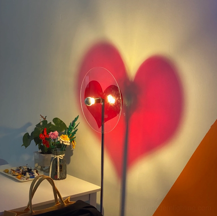 Deep red heart-shaped shadow cast by floor lamp from side angle, showing polished chrome metal pole in home office