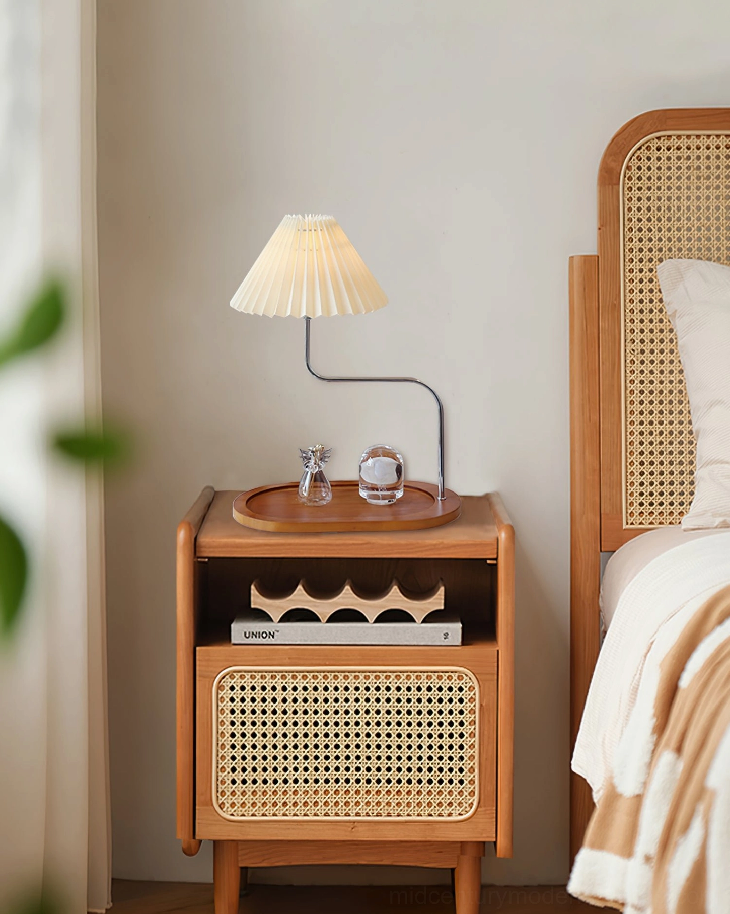Mid-century modern pleated lamp positioned on rattan bedside cabinet in bedroom setting