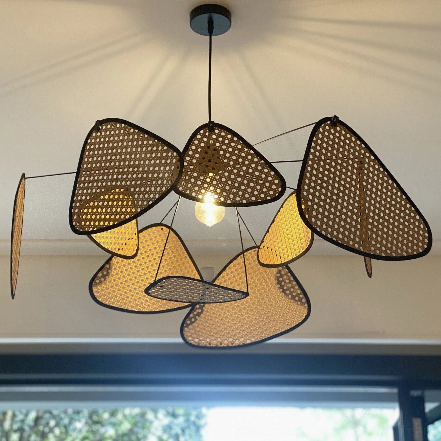 Modern rattan chandelier close-up side view, perforated bamboo panels with black metal edges, exposed central LED bulb