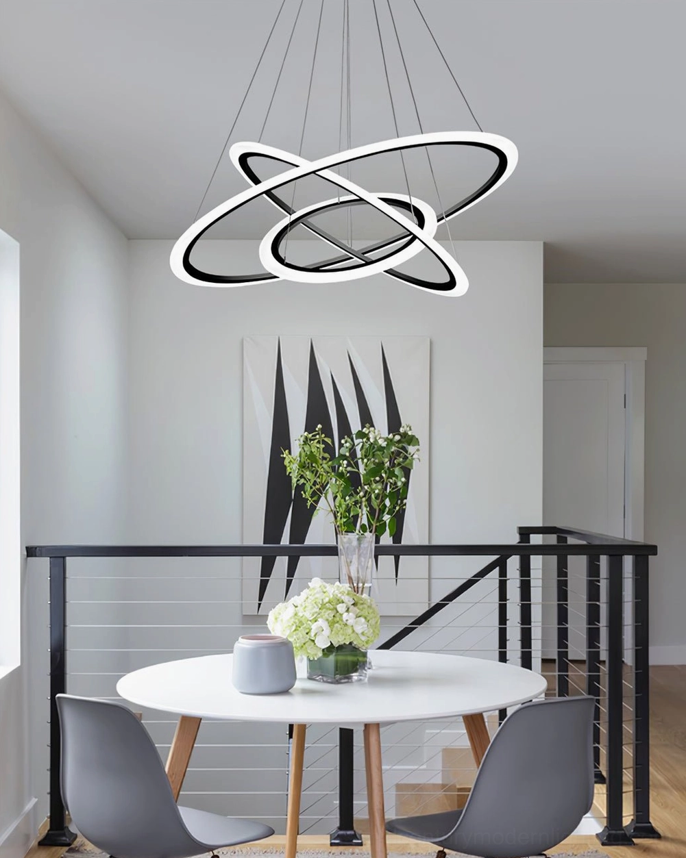 Three-ring LED chandelier suspended above contemporary dining area with black railings and green floral table decor