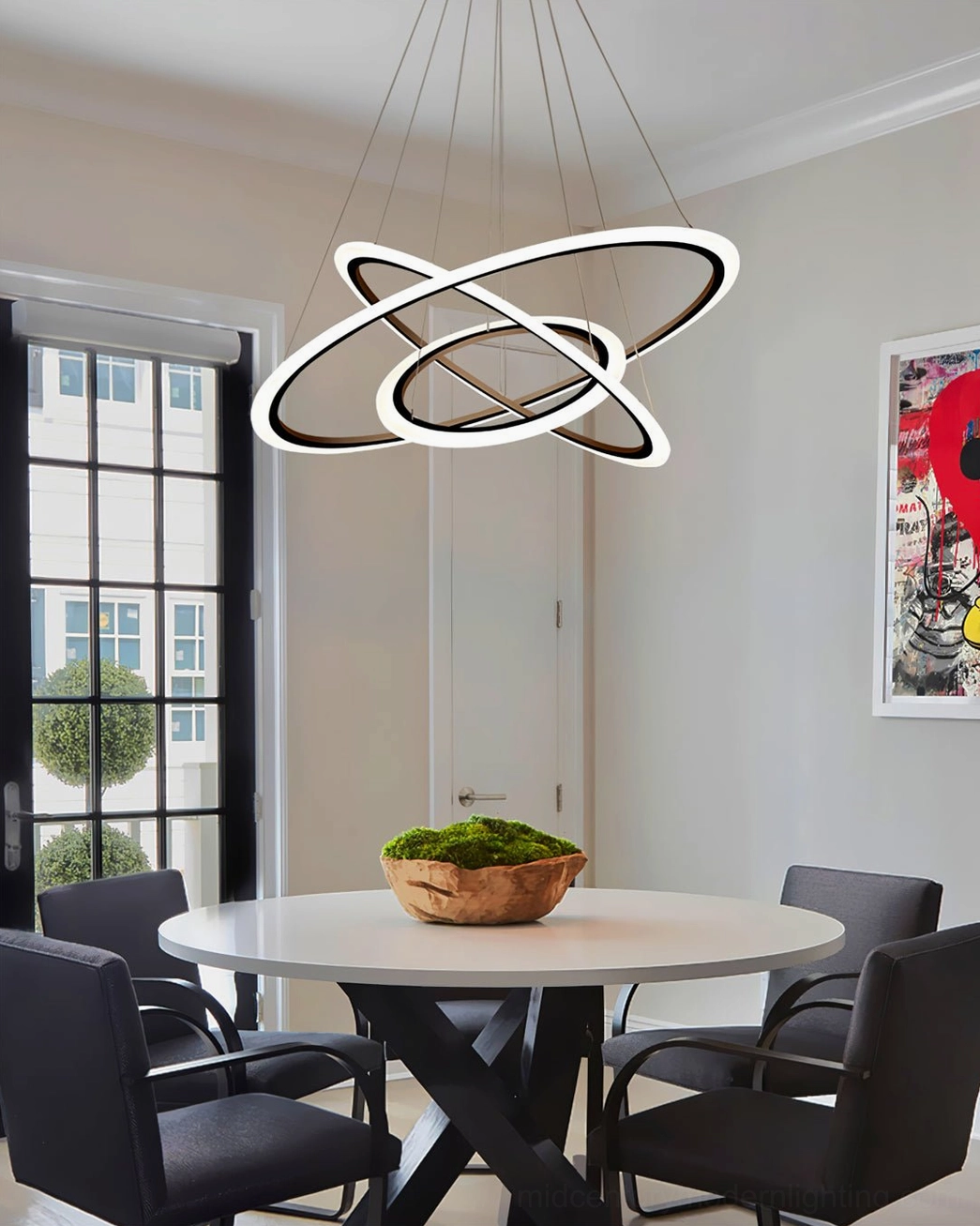 Intersecting ring chandelier suspended above bright dining nook beside large window with wooden plant decor