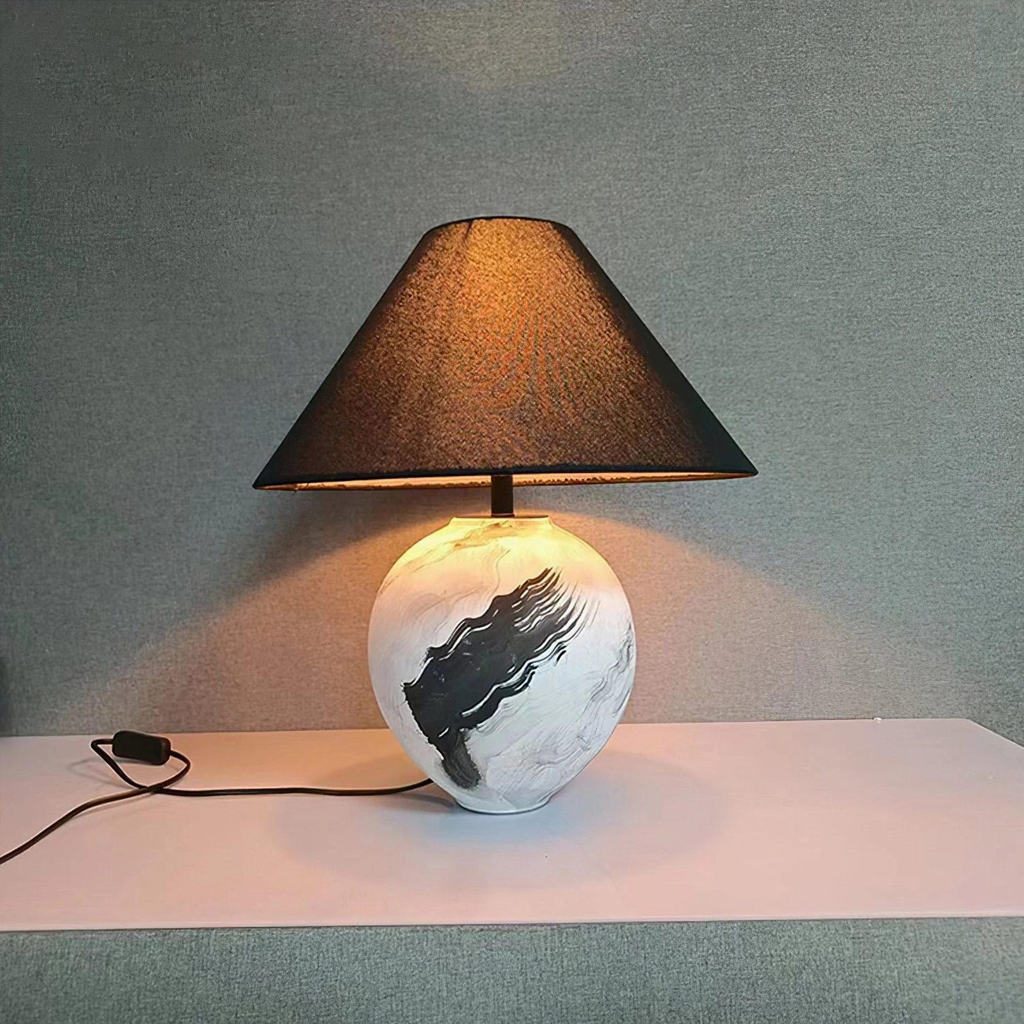 Illuminated ceramic table lamp with glowing white linen shade showing warm interior light on minimalist tabletop