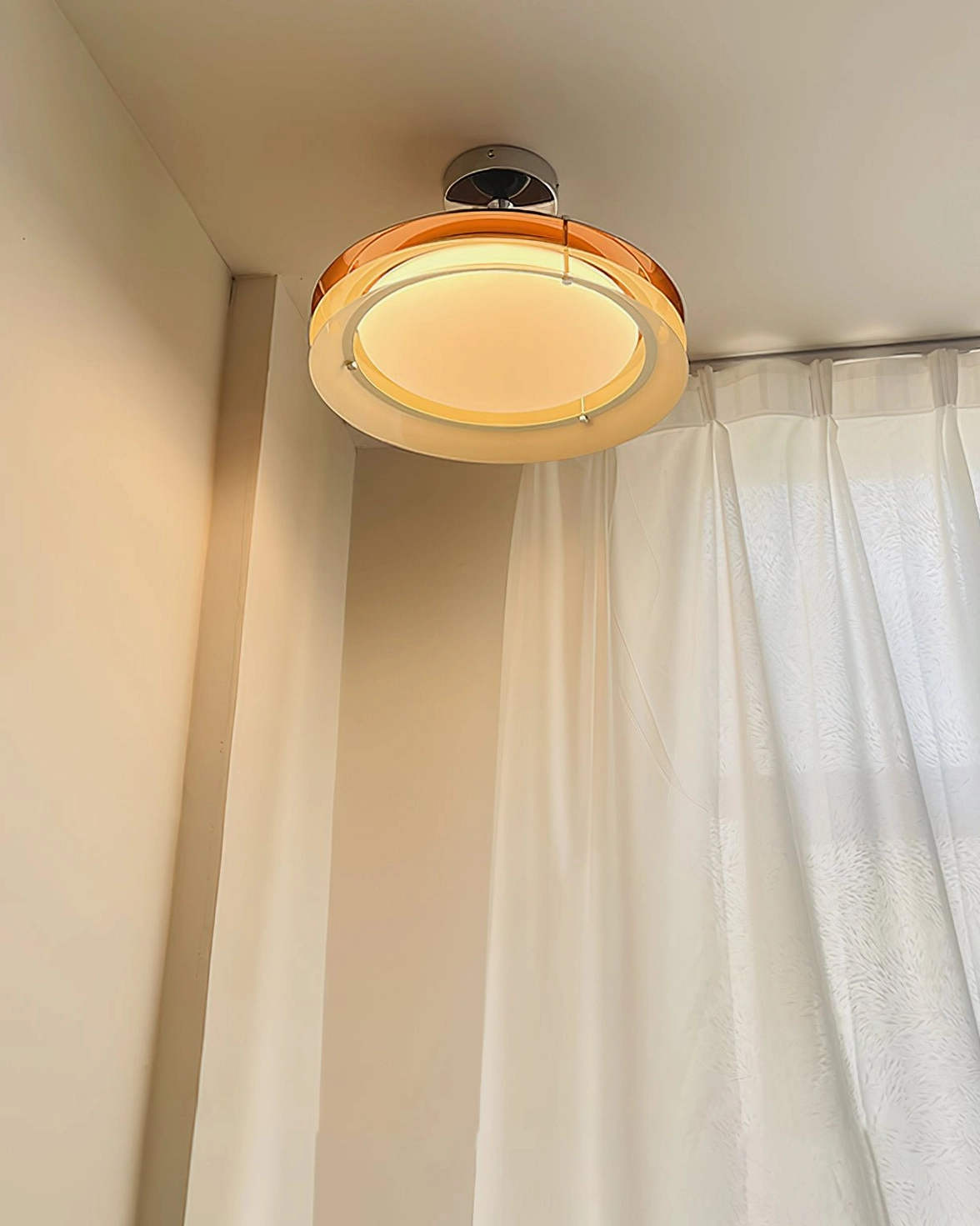 Compact 40cm Moers ceiling lamp installed in bedroom with sheer white curtains emitting warm ambient light with amber frame