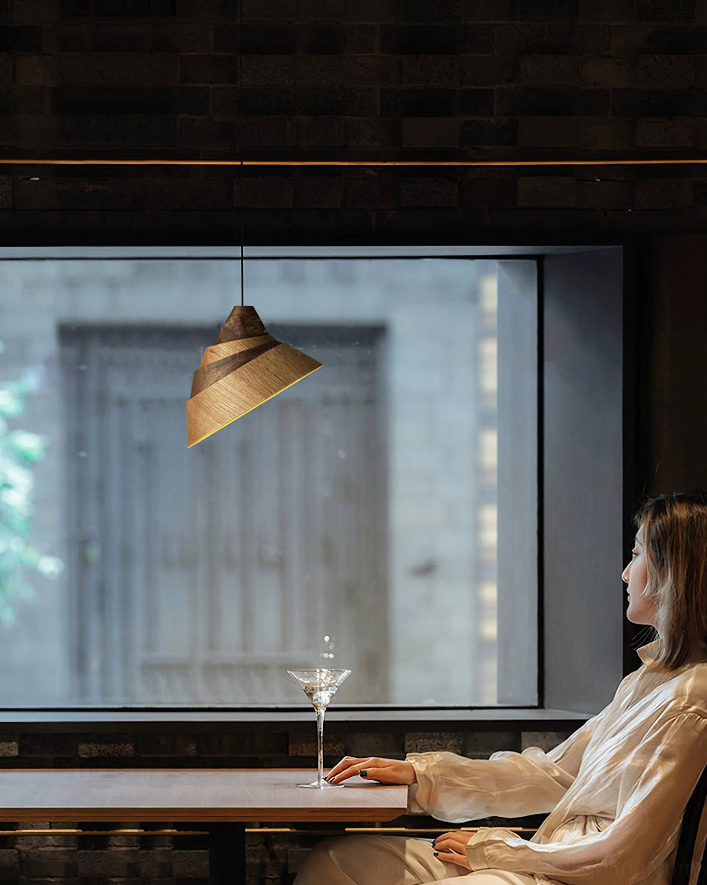 Tilted conical wooden pendant lamp in cozy cafe dining setting with warm ambient lighting and female customer at table