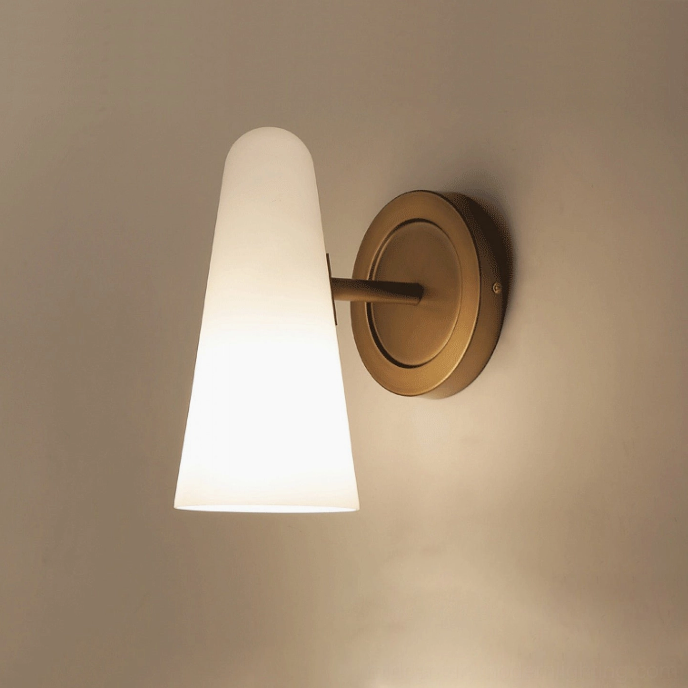 Single Montfaucon cone wall sconce angled side view with solid brass round mount and soft warm lighting