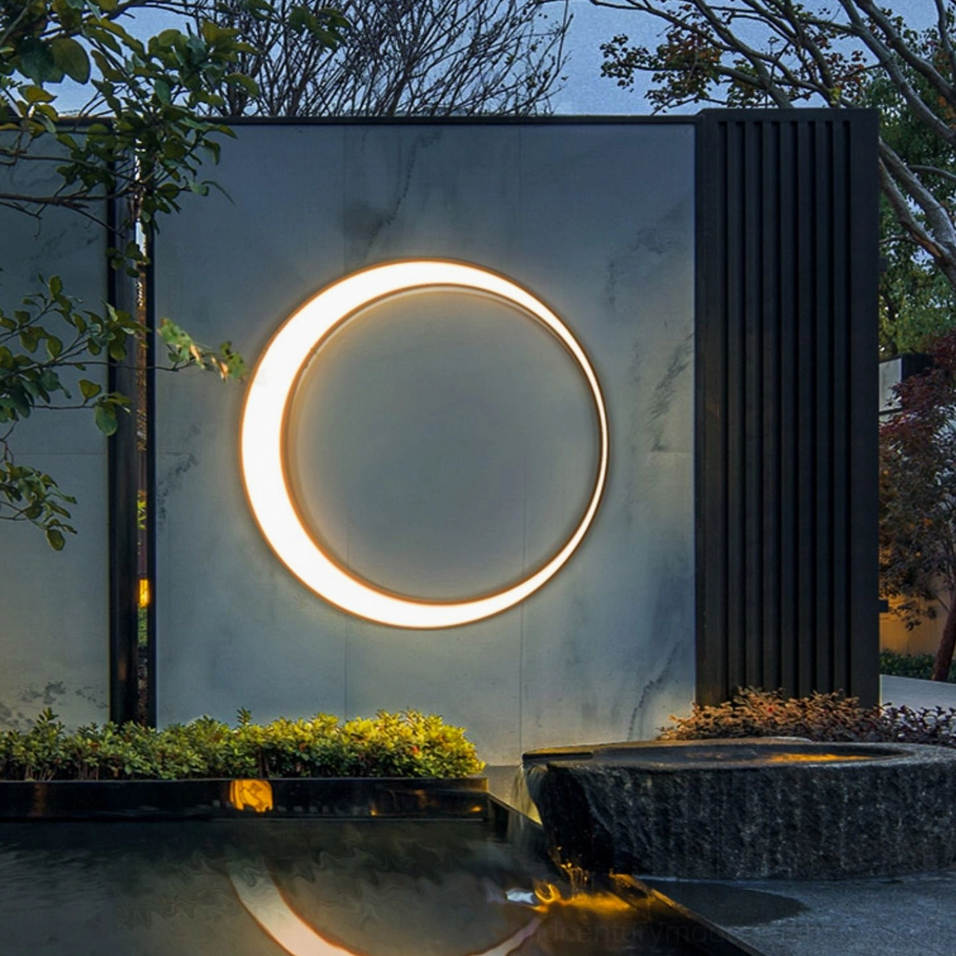 Contemporary outdoor wall lamp illuminated on modern waterscape courtyard exterior showing warm LED glow and minimalist ring silhouette