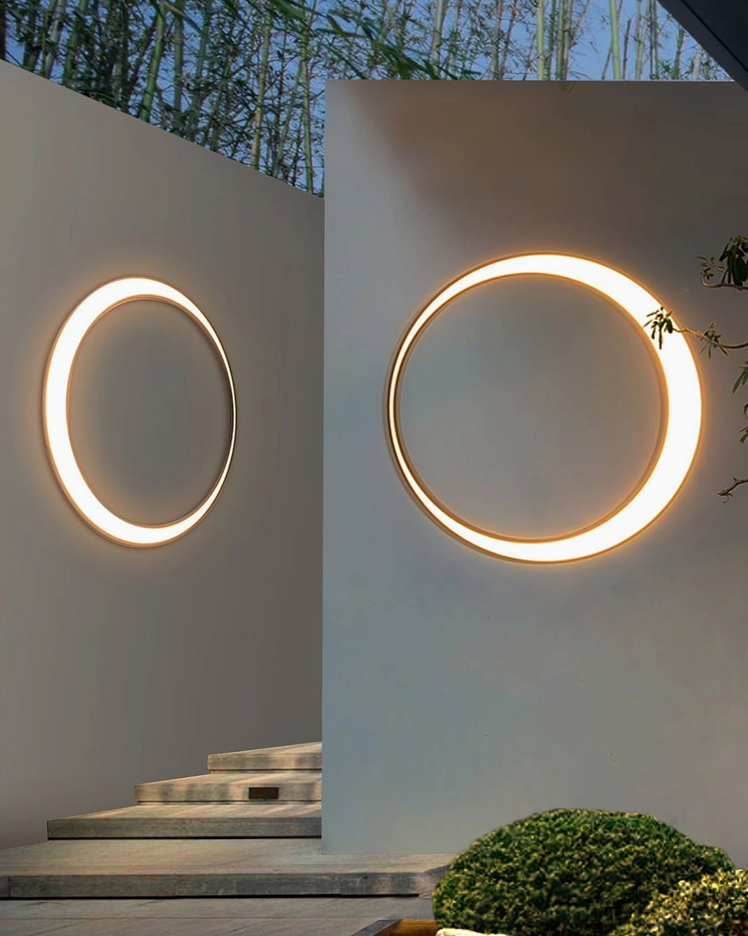 Two different sized circular outdoor wall lamps with warm trim on courtyard stone steps showcasing compact and statement size options