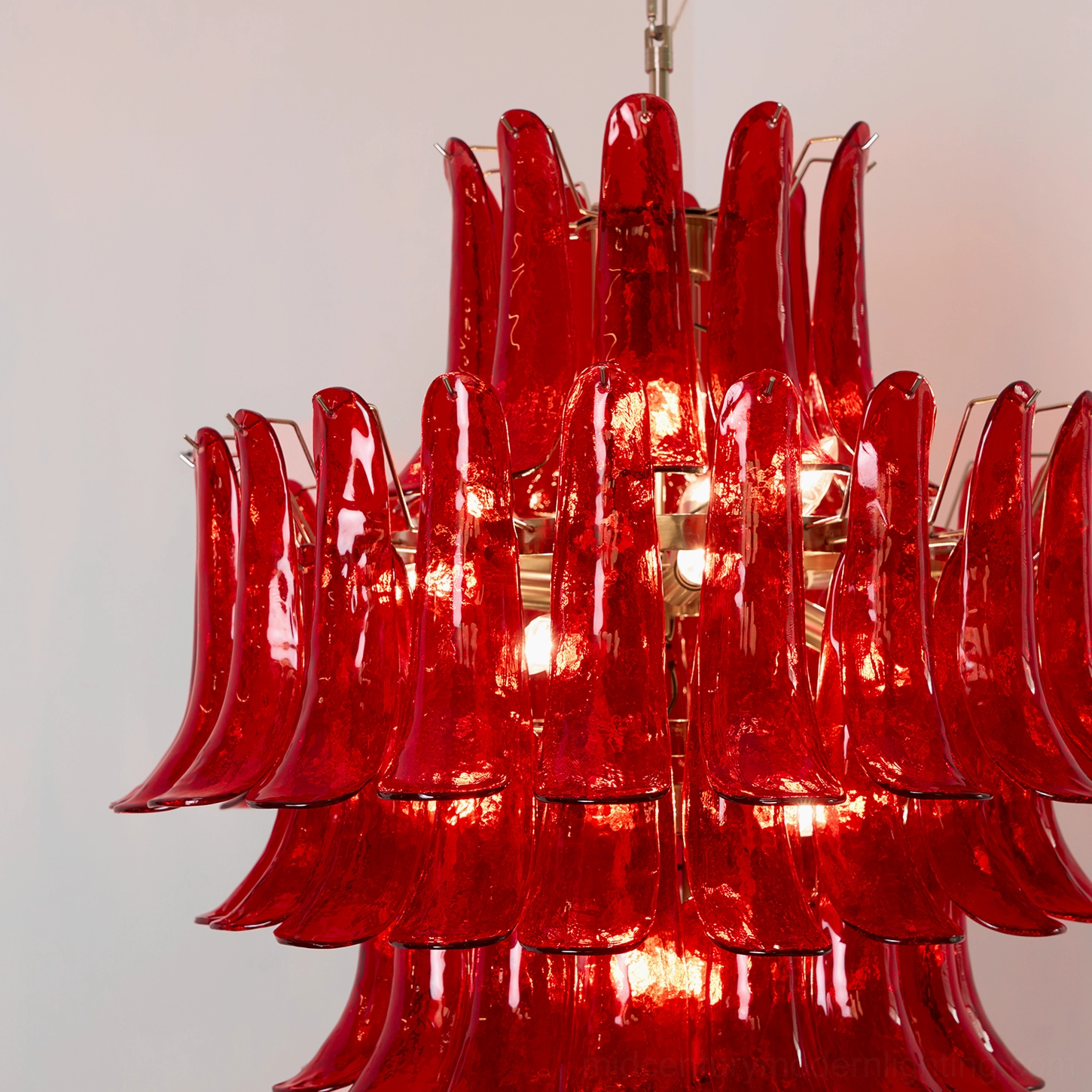 Close-up frontal view of illuminated Murano glass chandelier with multiple glowing bulbs and clustered red glass petals creating dramatic light effect