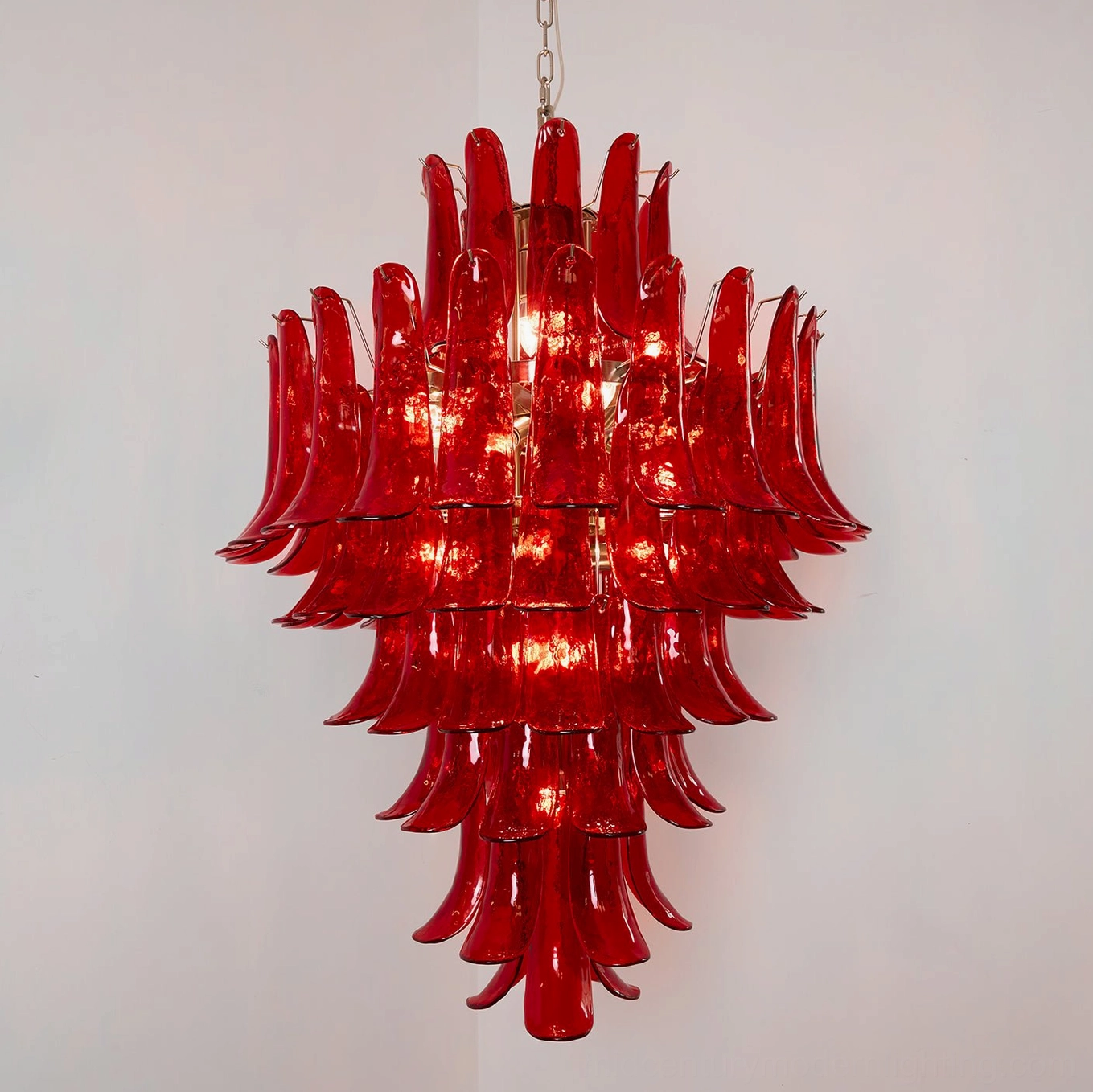 Illuminated crimson Murano glass chandelier with internal bulbs glowing, displaying tiered petal structure and light refraction properties