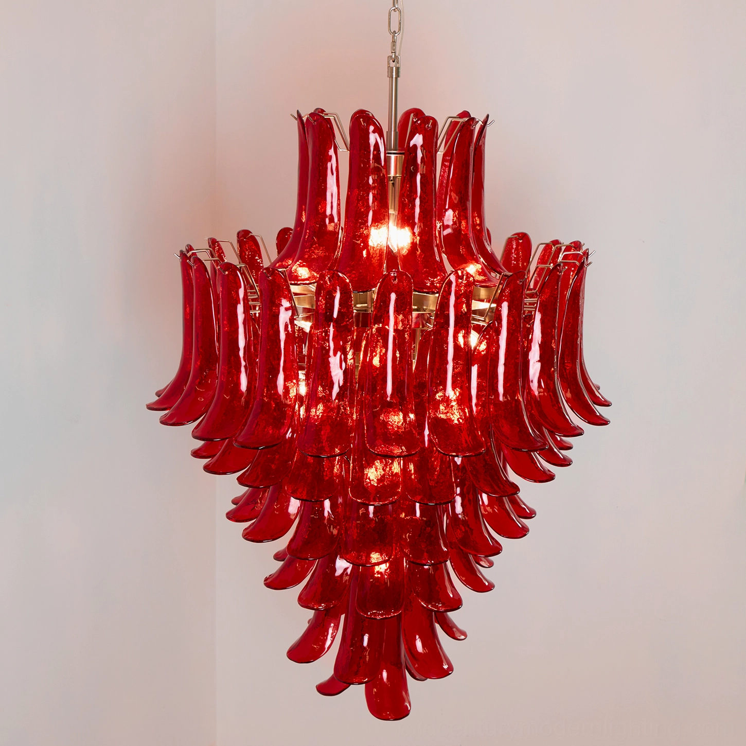 Glowing Murano glass chandelier installed in corner of room, showing central light emission through layered red glass petals