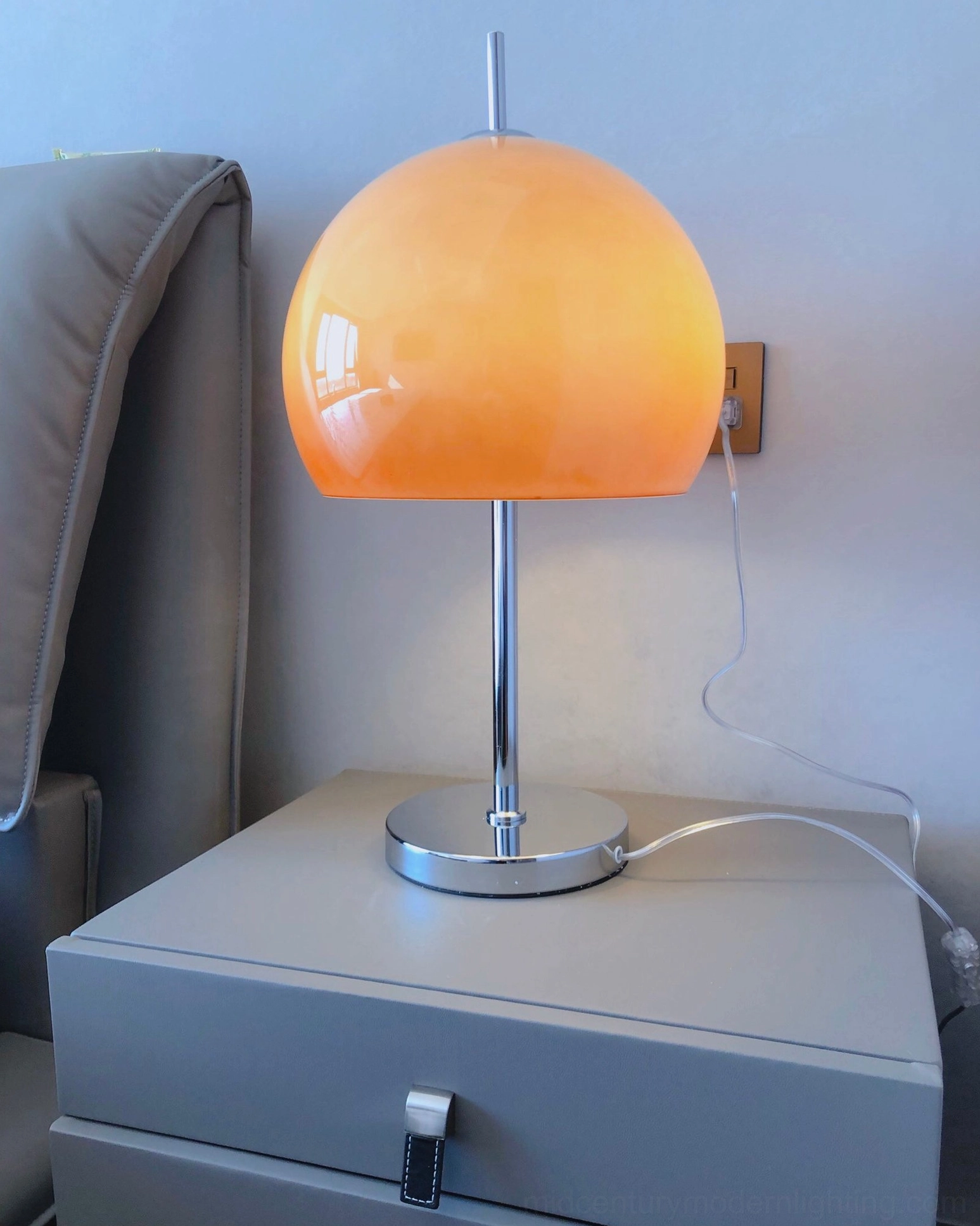 Mushroom table lamp with orange gradient acrylic shade in bedroom bedside setting with wall-mounted socket