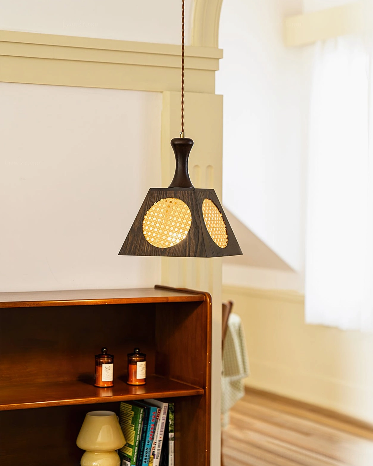 Mysore handwoven rattan pendant lamp glowing in warm vintage living room with wooden shelving, showing full light diffusion effect