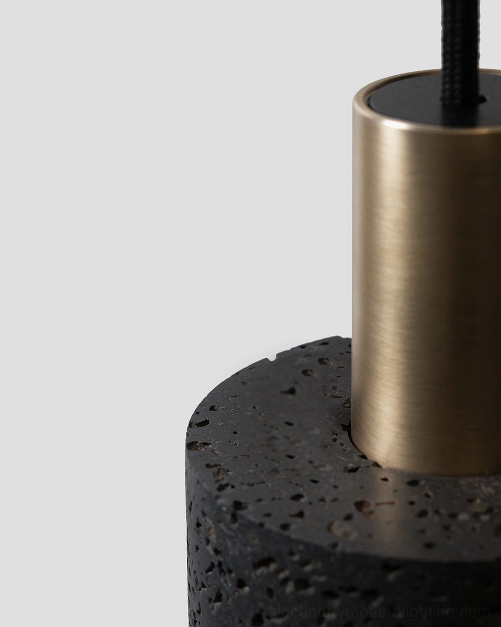Low-angle close-up of N Stone Pendant Lamp showing brushed brass collar detail and rough volcanic stone surface texture