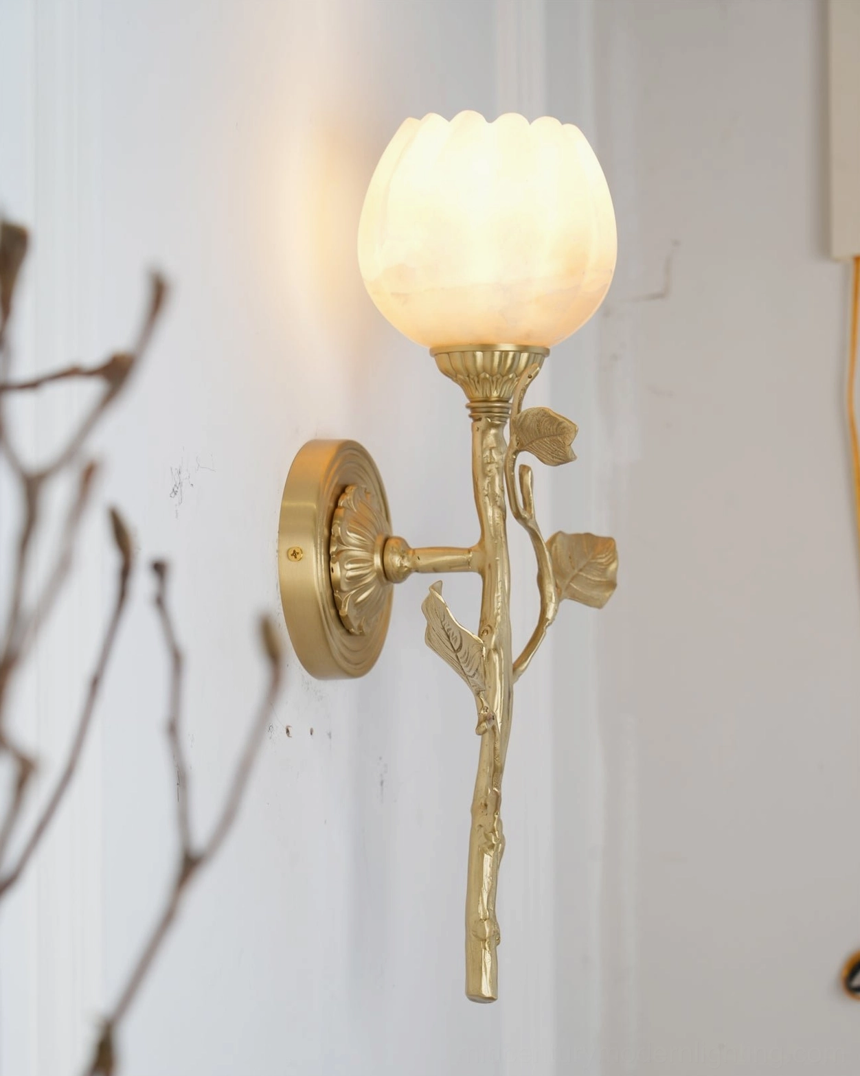 Side view of Natalia alabaster wall sconce mounted on interior wall with decorative dry branches styling