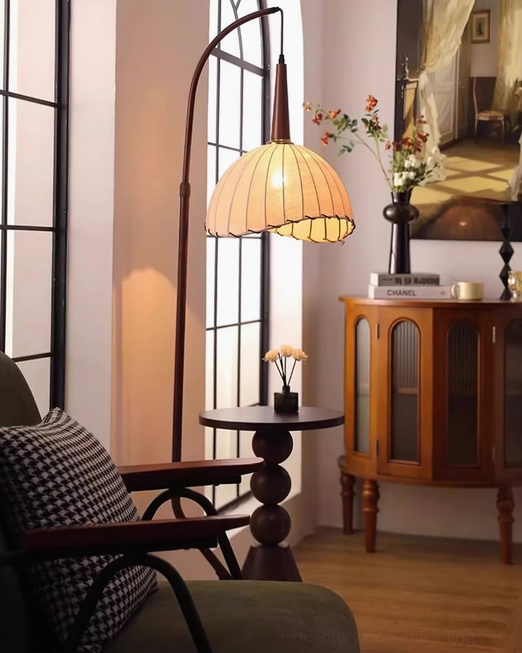Naumy arc floor lamp angled view in French vintage living room, warm lit beige shade with checkered pillow on green armchair