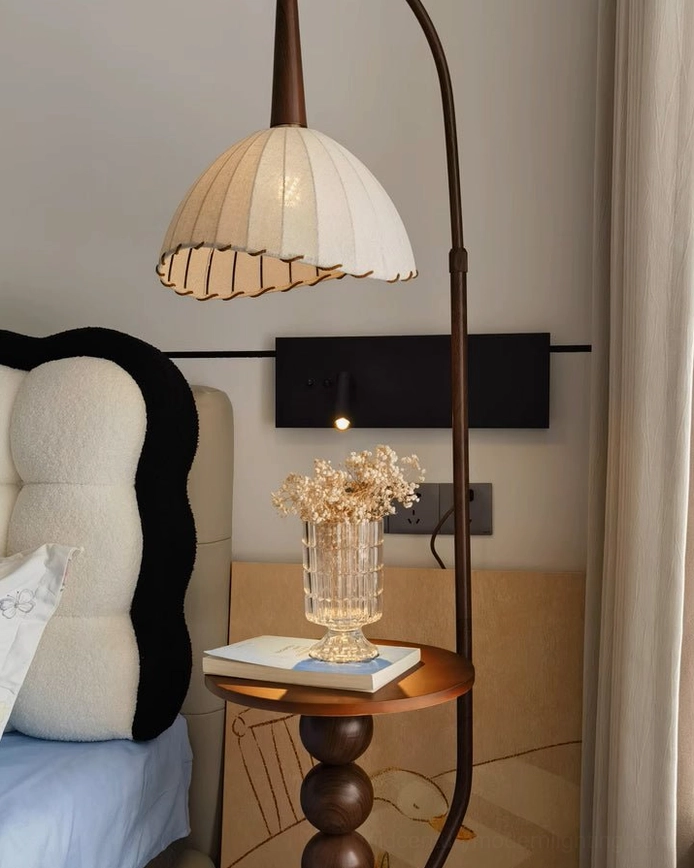 Naumy arc lamp eye-level view showing off-white pleated shade and wooden side table with dried flower arrangement