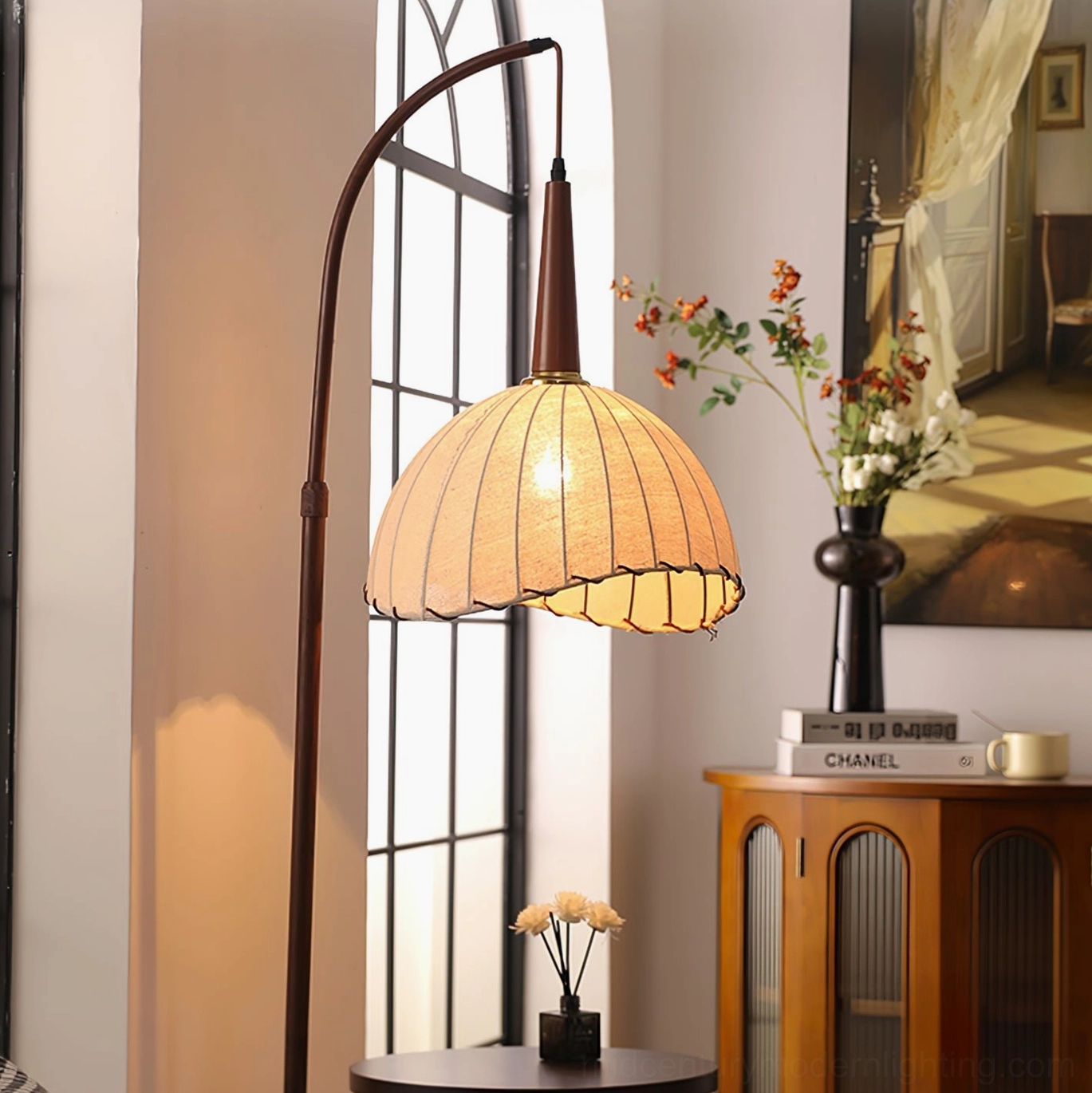 Close-up detail of Naumy lamp's glowing pleated linen shade with decorative floral arrangement in vintage interior setting