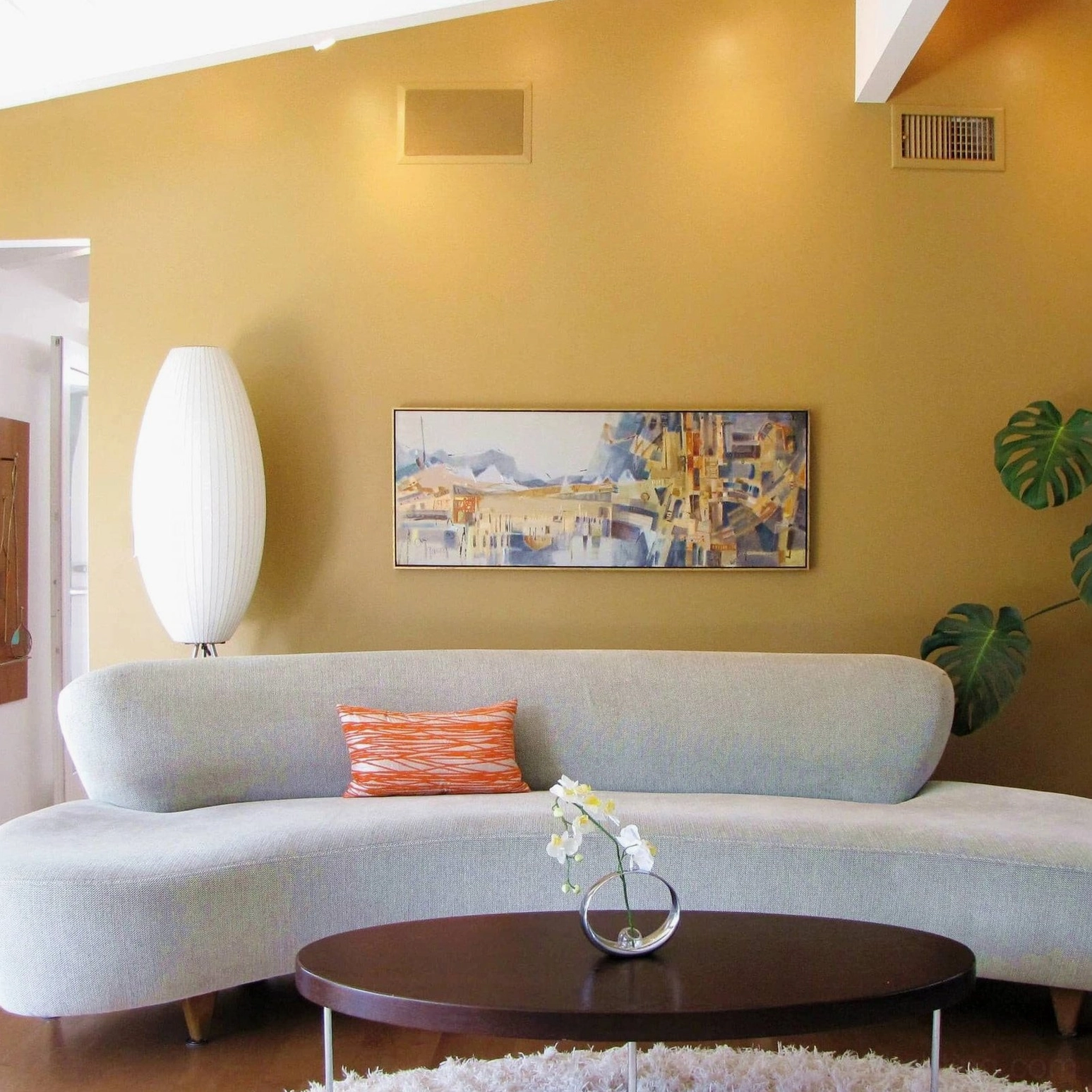 White George Nelson tripod floor lamp illuminating minimalist mid-century modern lounge with curved sofa and warm neutral decor