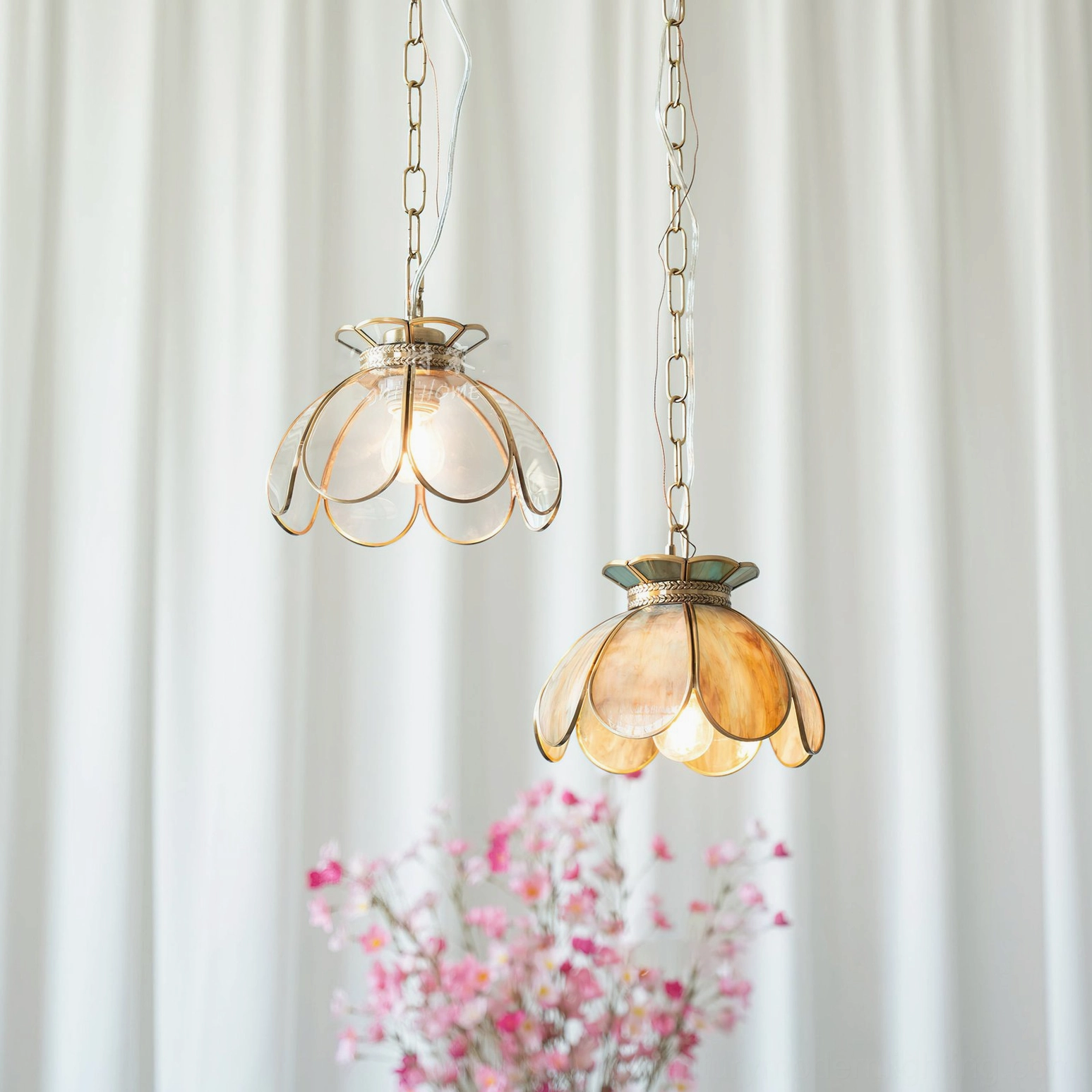 Vertical hanging display of Odette lotus pendant light pair in mixed colors against white curtain with pink florals
