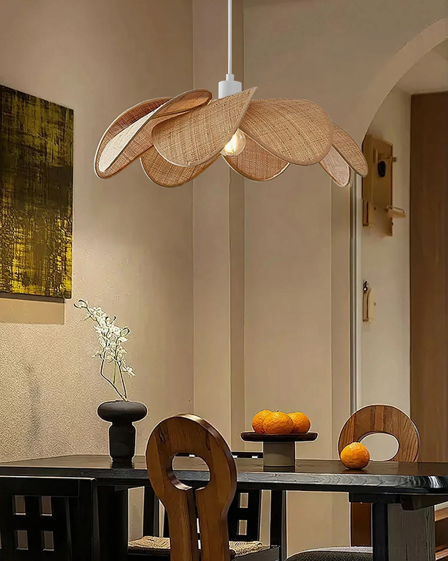 Odilia rattan pendant light above black dining furniture, minimalist neutral interior, three-quarter view showing refined metal fixture and layered petals