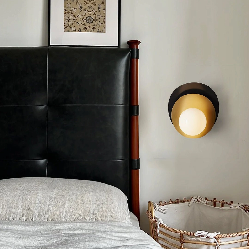 Side profile view of Olivia wall sconce with warm-lit spherical glass bulb and black brass finish in bedroom setting