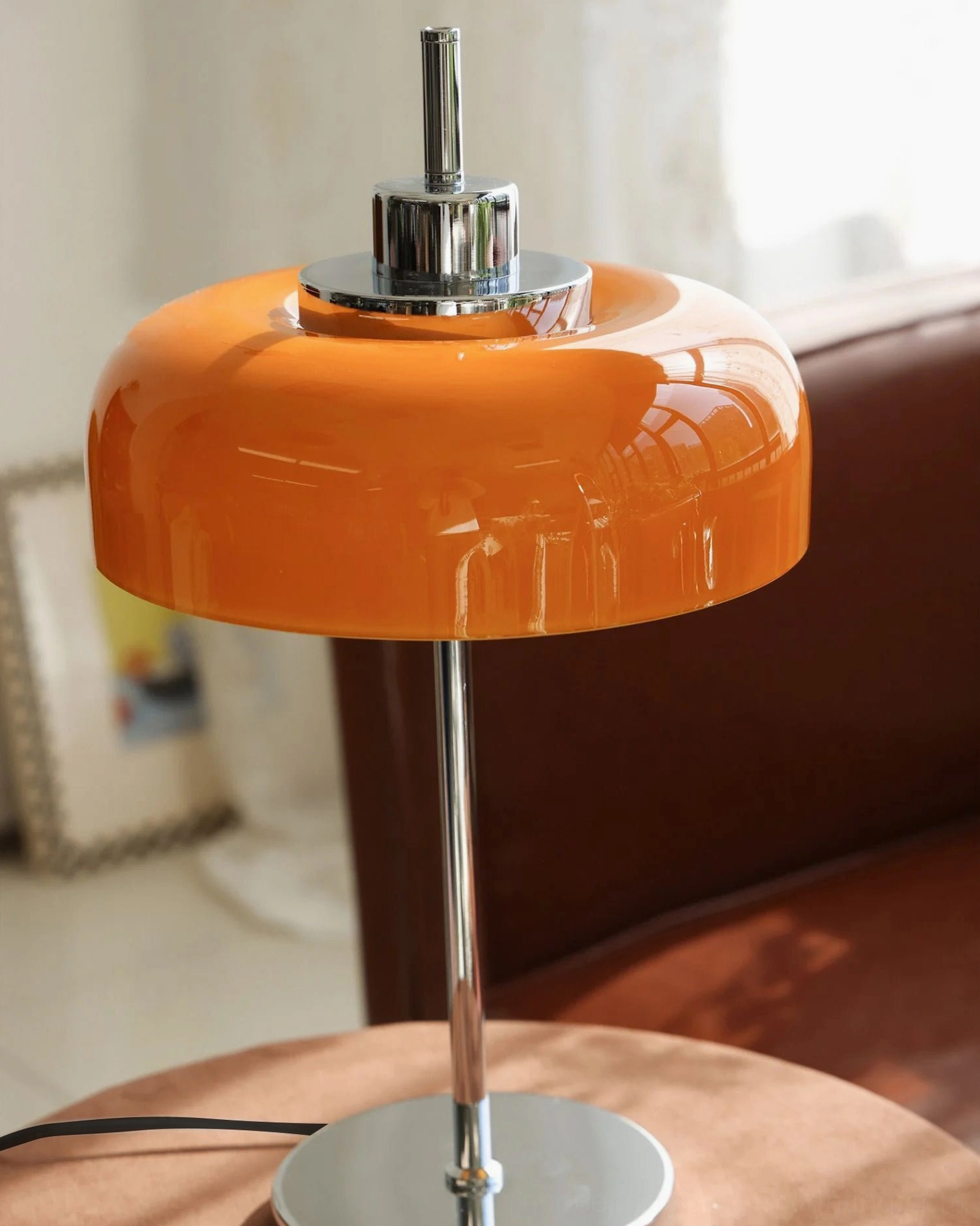 Close-up front view of retro orange table lamp showing dome shade detail with brown leather sofa backdrop