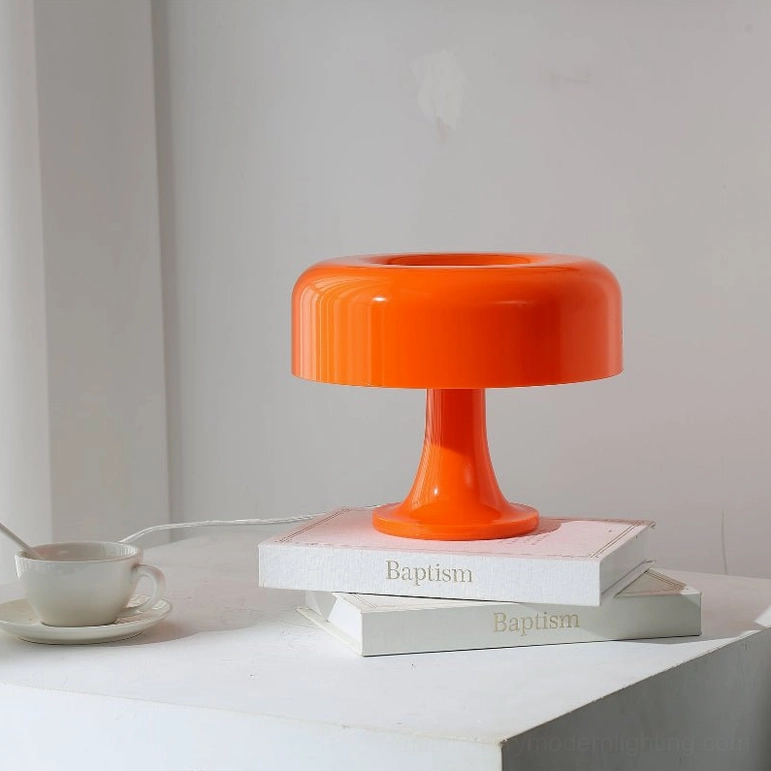 Orange mushroom table lamp front three-quarter view on white tabletop with stacked books and coffee cup decor