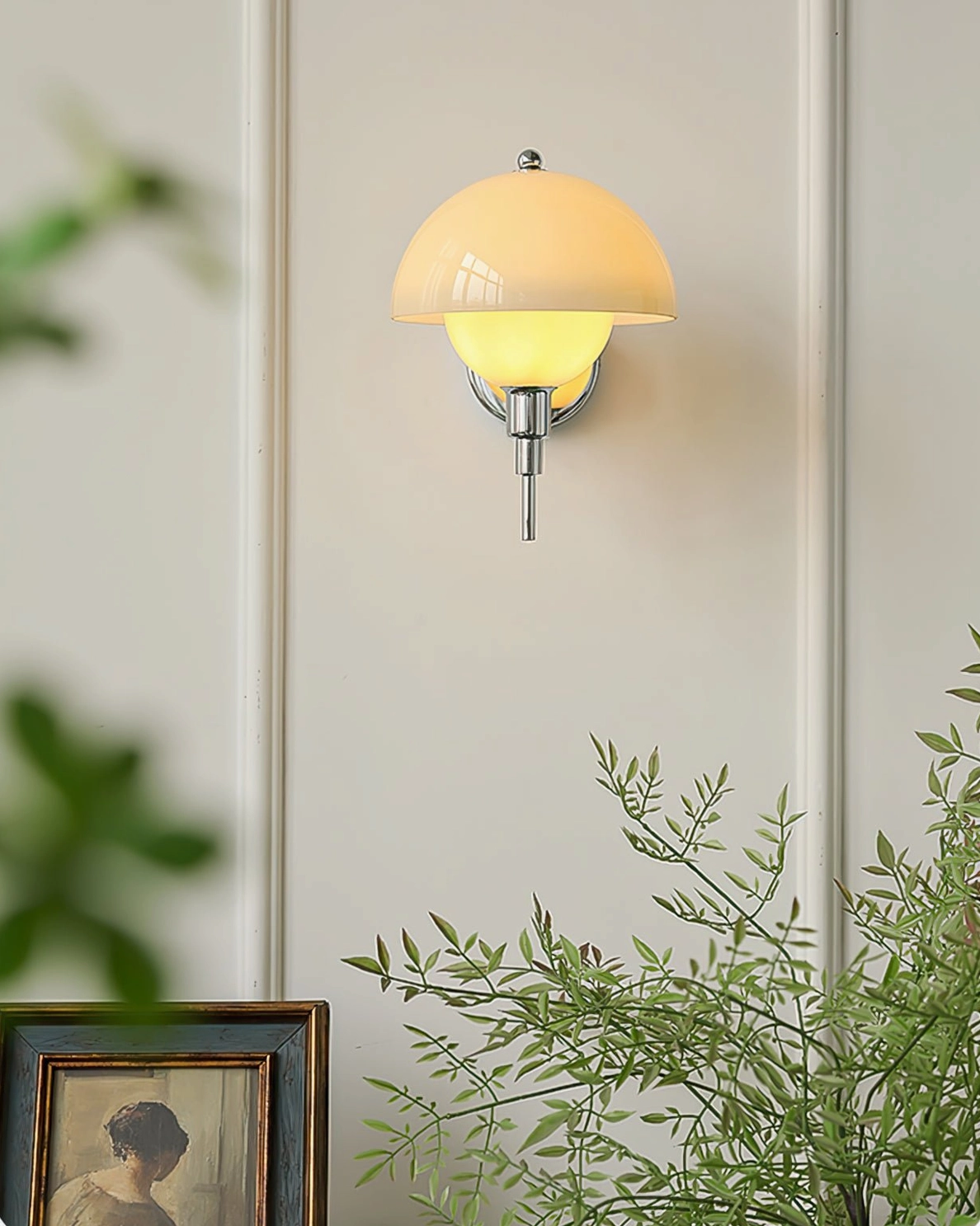 Distant view of light amber anchored orb wall lamp mounted on home wall with framed artwork and foliage