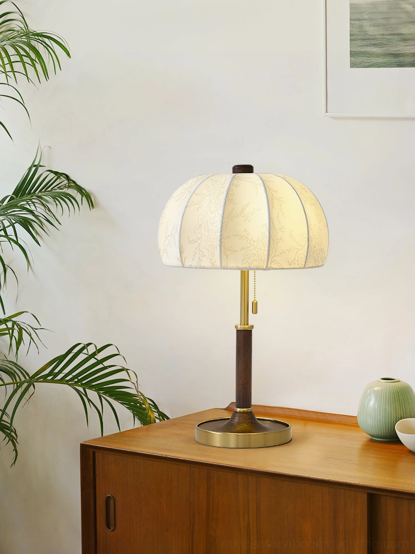 Beige pumpkin fabric shade table lamp with brass base on Japanese wooden cabinet with green plants