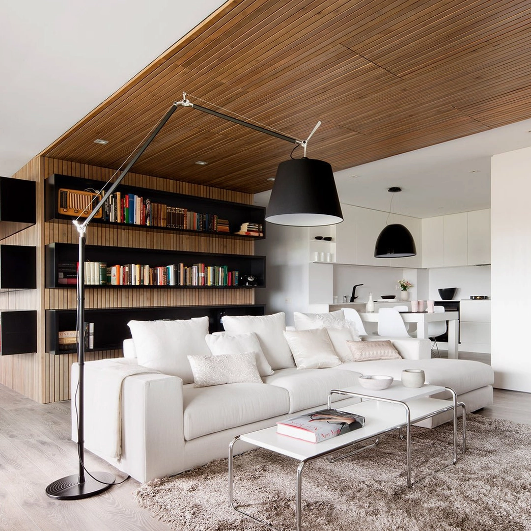 Oversized swing arm floor lamp with black conical shade in double-height modern room with bookshelves, dramatic lighting
