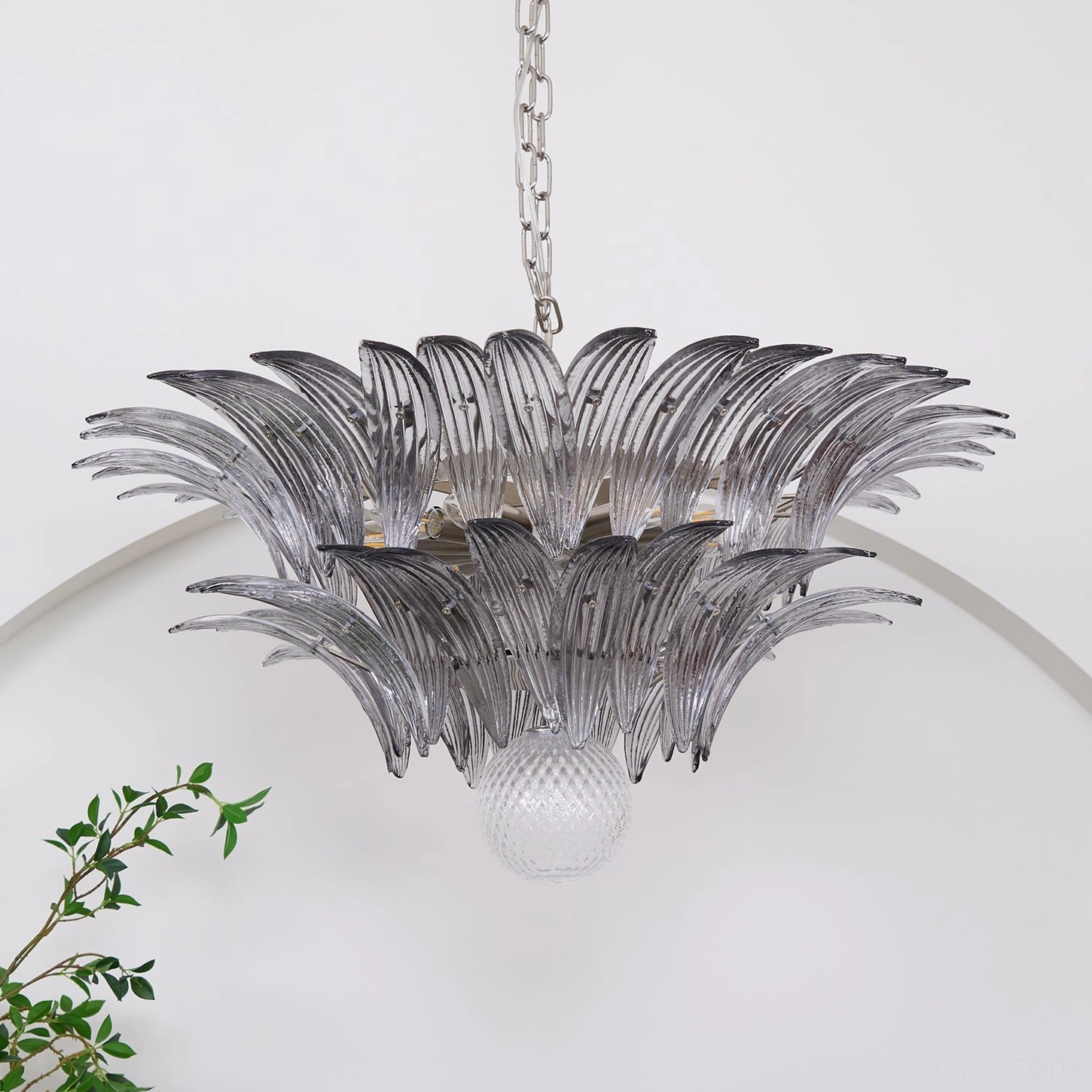 Close-up view of Murano glass palm leaf chandelier with silver chain suspension in minimalist modern interior with plants