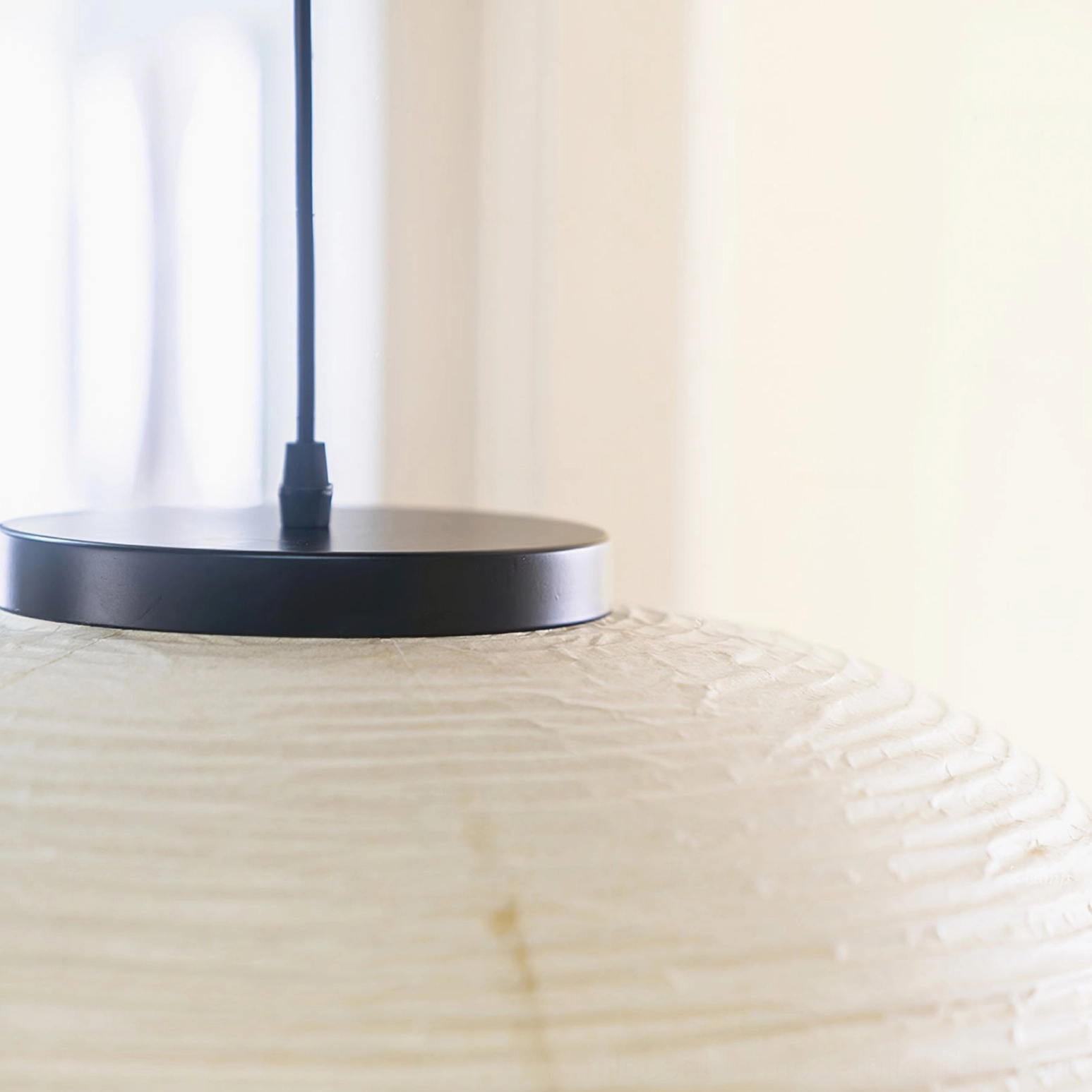 Pendant lamp detail shot – black metal canopy and suspension cord with textured paper shade