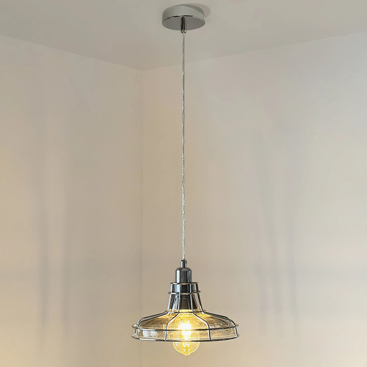 Williston pendant light in full hanging position showing long suspension cord and illuminated industrial design against bare wall
